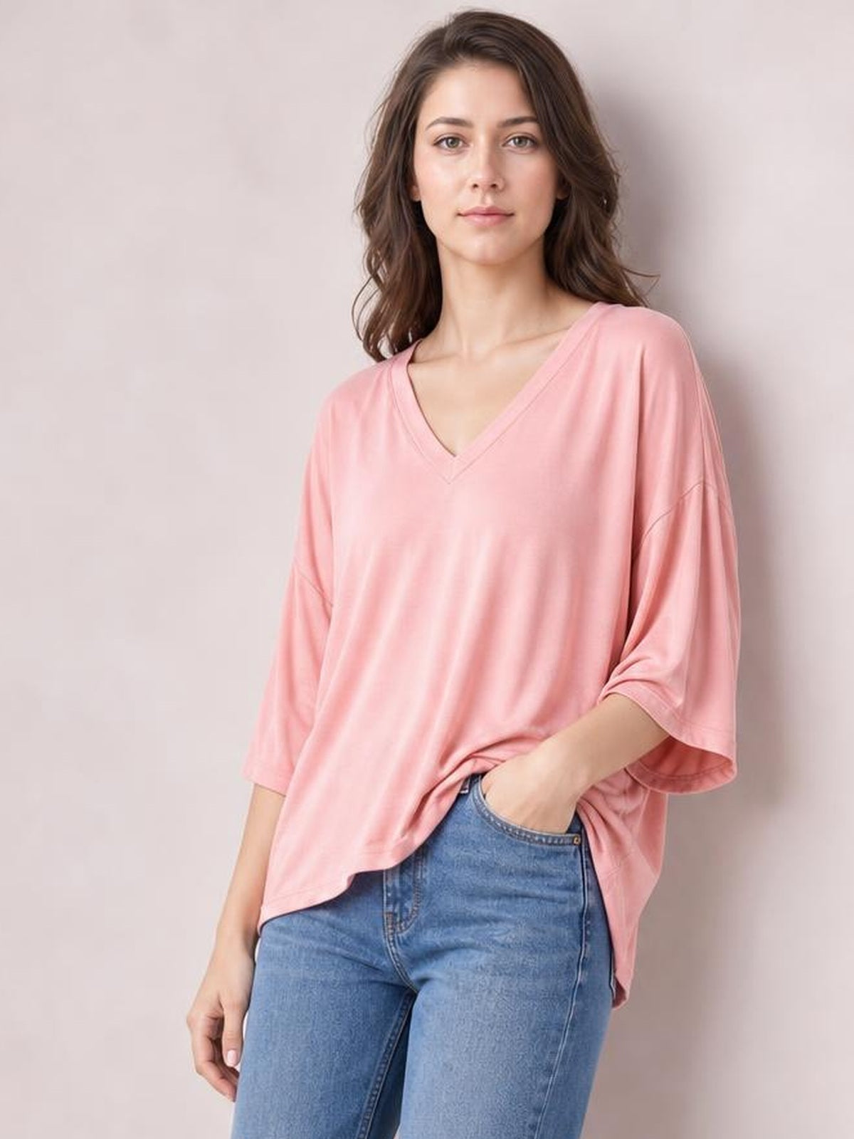 A woman stands in a relaxed pose wearing a pink bamboo V-neck drop shoulder T-shirt with loose sleeves, a curved hem, and an oversized silhouette.