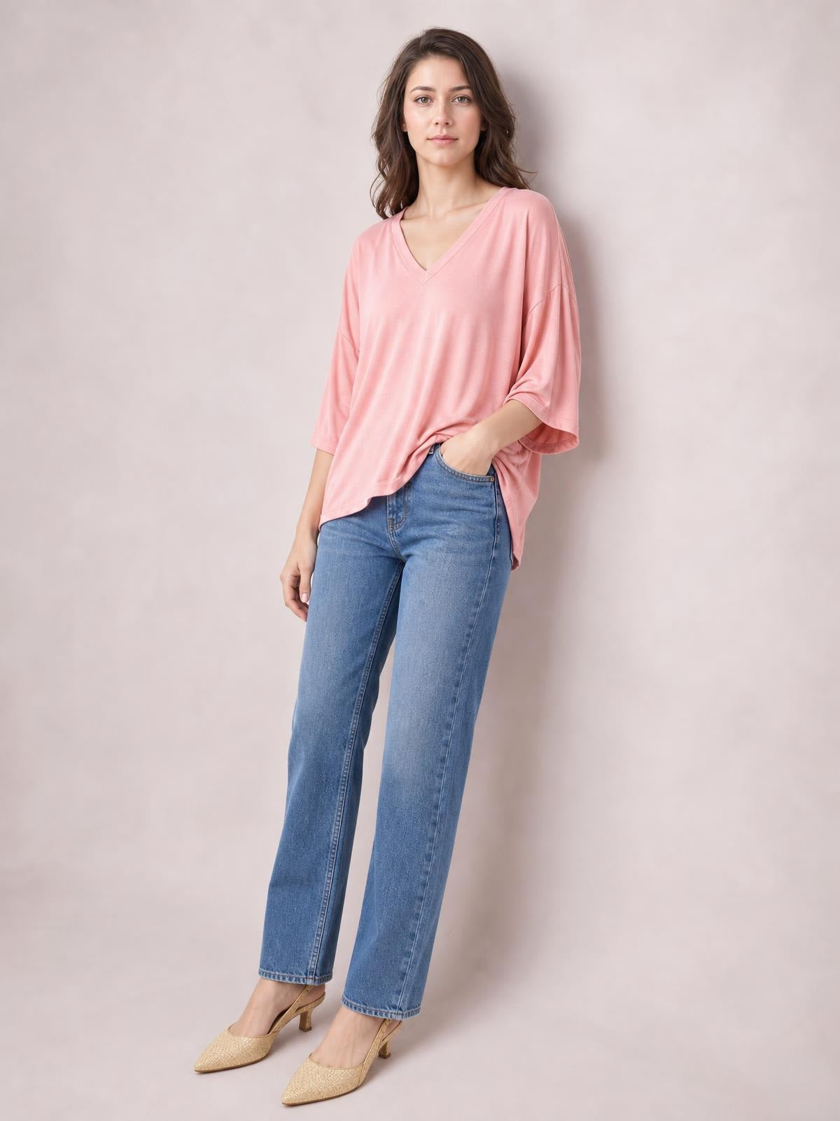A model poses in a pink bamboo V-neck drop shoulder T-shirt with a relaxed oversized silhouette, loose elbow-length sleeves, and a curved hem.