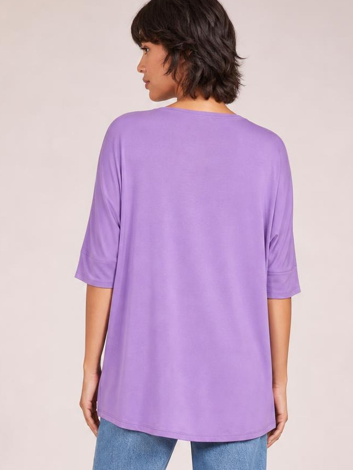 Model shown from behind wears a lavender bamboo T-shirt with a relaxed drop-shoulder silhouette, short sleeves, and a softly curved hem.