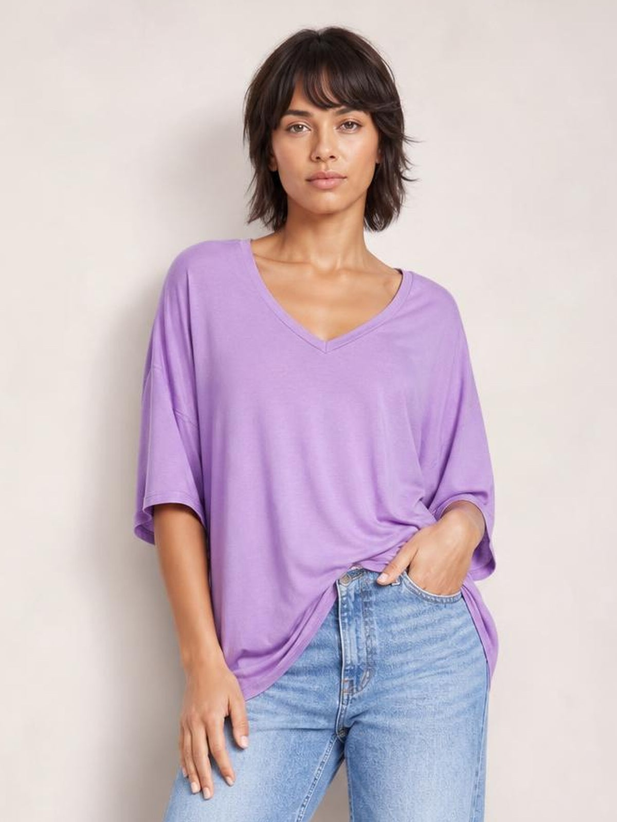 Model wearing a lavender bamboo V-neck T-shirt with drop shoulders, relaxed oversized silhouette, and loose short sleeves, posing with one hand in her jeans pocket.