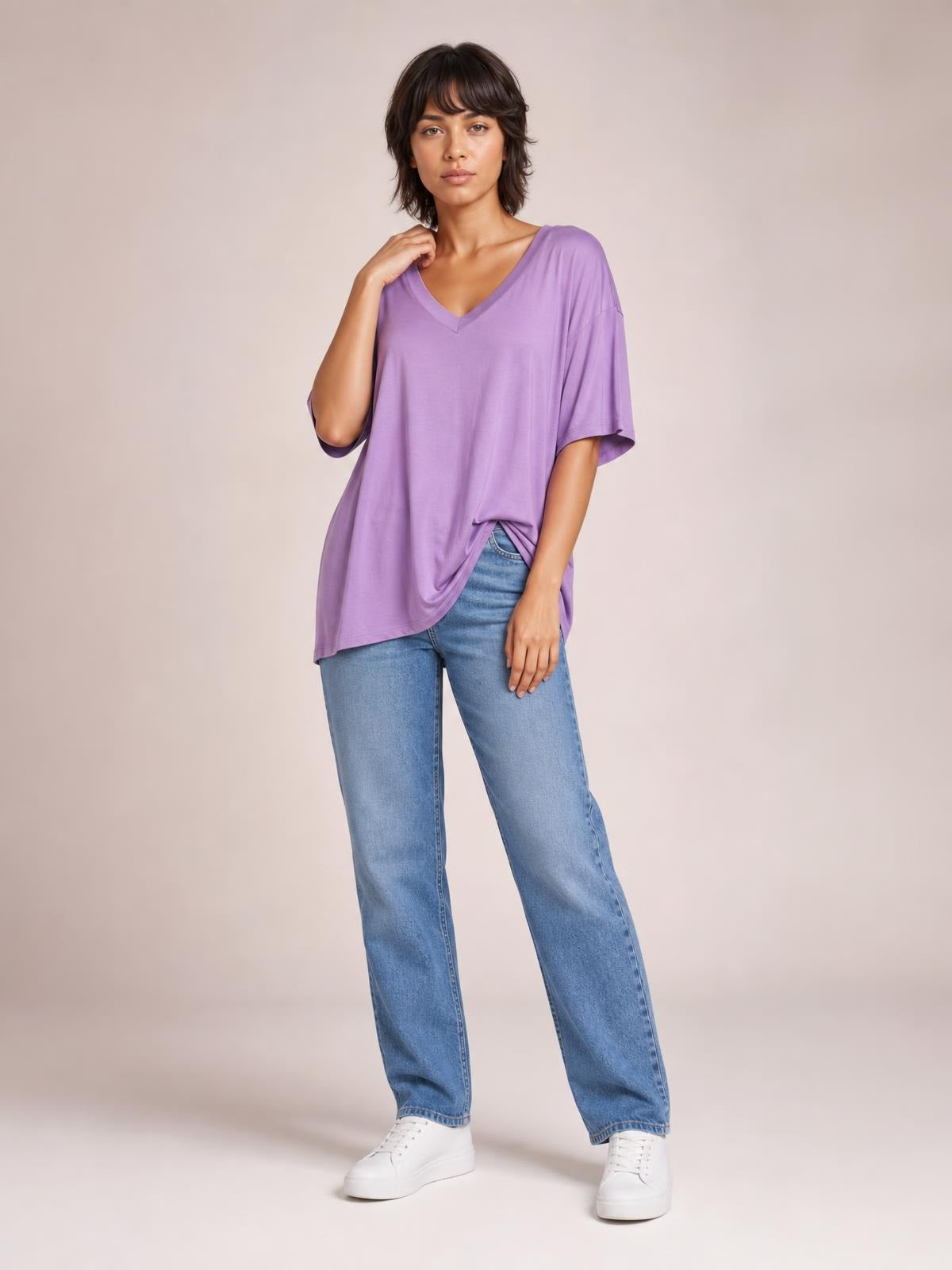 A model poses in a relaxed lavender bamboo V-neck T-shirt with drop shoulders, short sleeves, and an oversized silhouette, one hand touching the neckline.