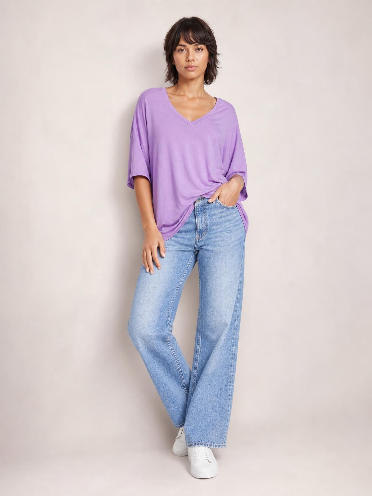 Model poses in a relaxed lavender Bamboo V-Neck Drop Shoulder T-Shirt with a loose silhouette, wide sleeves, and a front tuck into light-wash jeans.