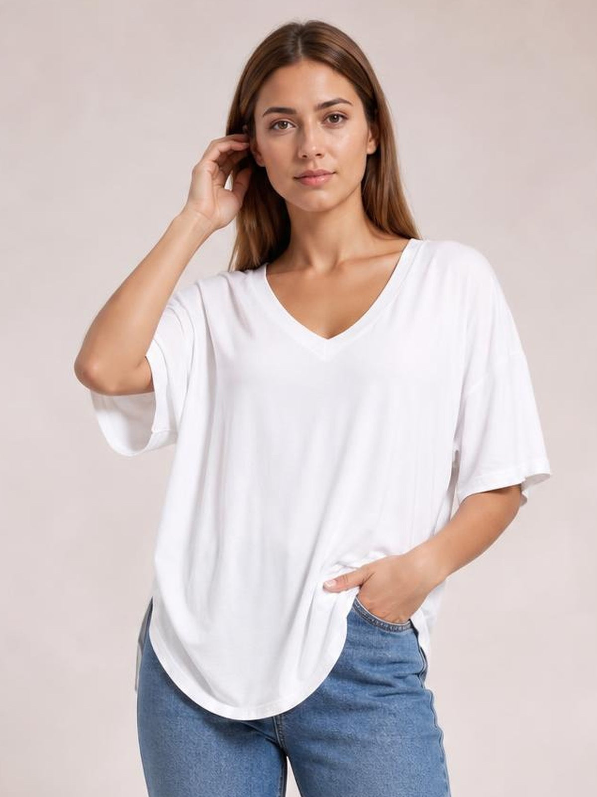 Model poses in a white bamboo V-neck drop shoulder T-shirt with a relaxed oversized silhouette, short sleeves, and curved hem.