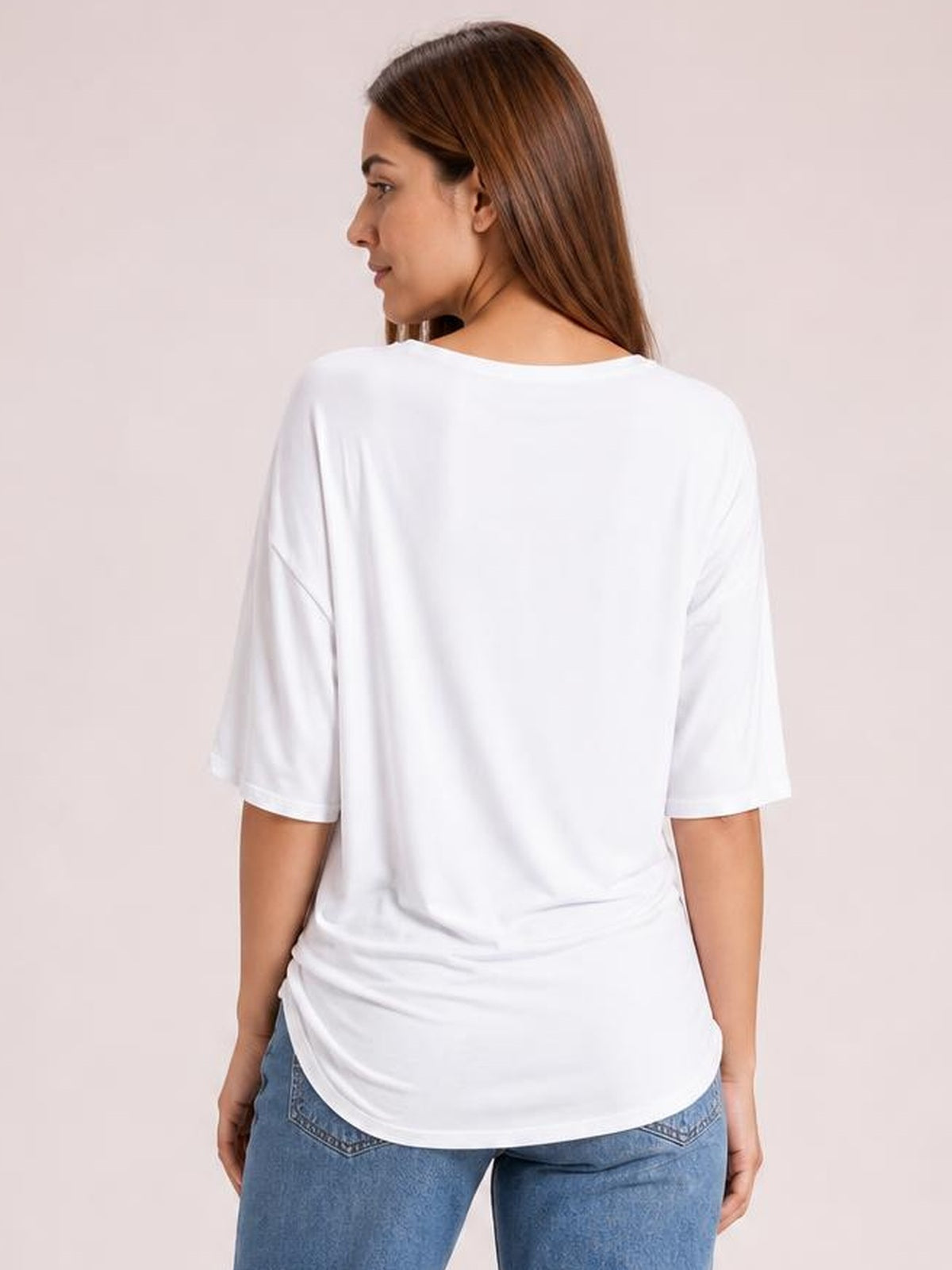 Model looks over her shoulder wearing a white drop-shoulder T-shirt with relaxed short sleeves, a loose silhouette, and a rounded hem.