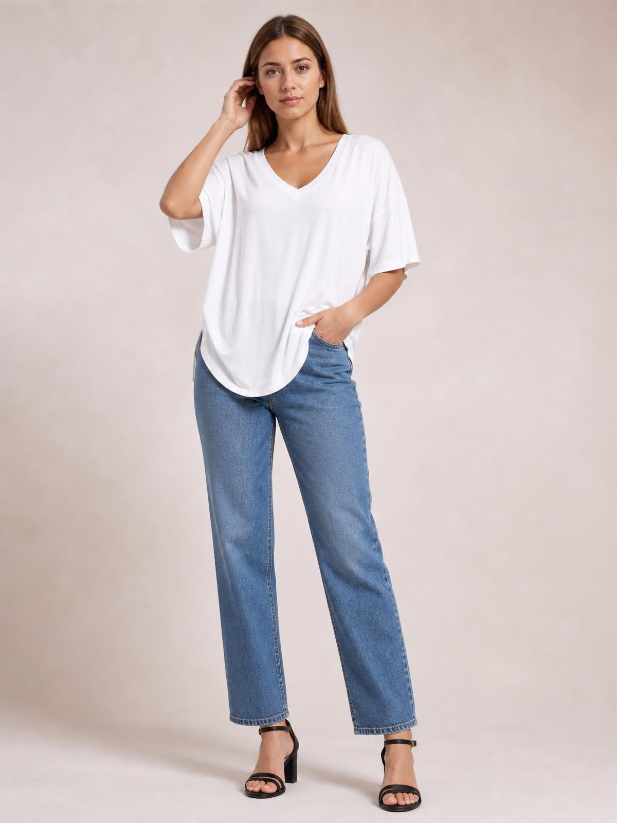 A model poses in a white bamboo V-neck T-shirt with drop shoulders, relaxed short sleeves, a curved hem, and an oversized silhouette over jeans.