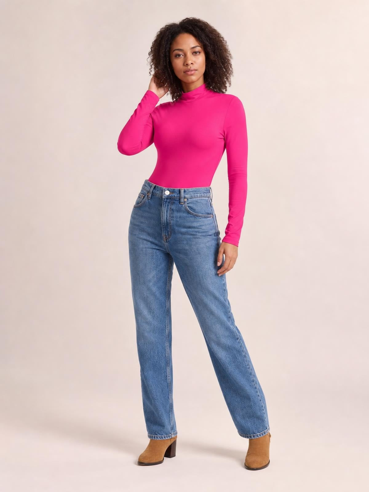 Model wears a bright pink mock neck long sleeve bodysuit with a fitted silhouette and moderate stretch, posing with one hand in her hair.