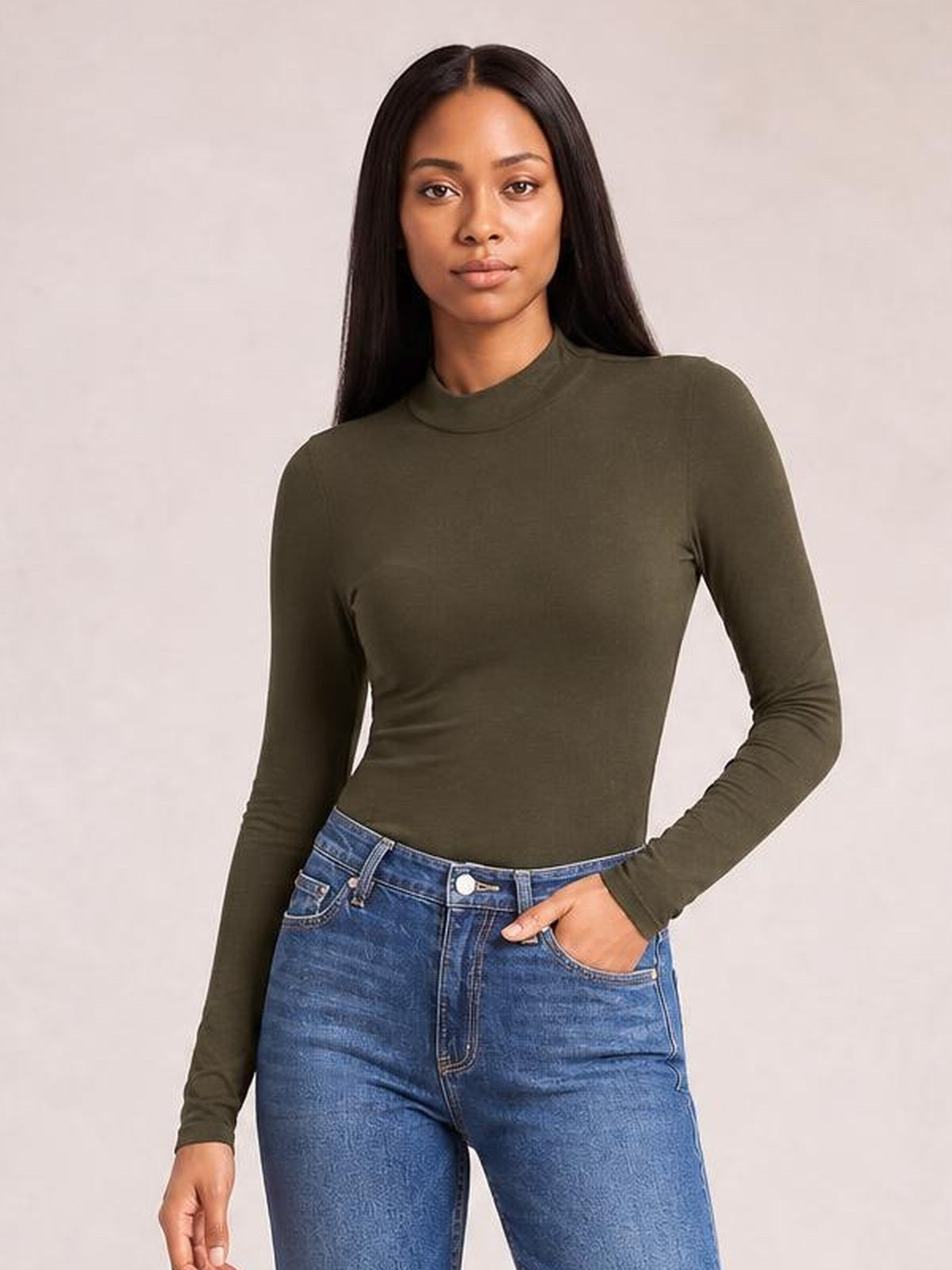 Model poses in a fitted olive green mock neck bodysuit with long sleeves and a smooth, opaque silhouette, paired with jeans.