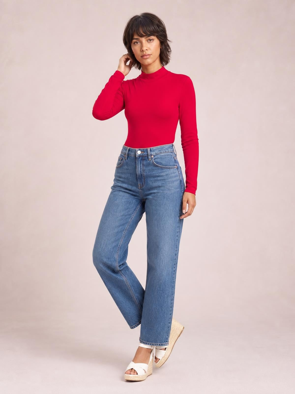 Model wears a bright red mock neck long sleeve bodysuit with a smooth, fitted silhouette, posing with one hand near her hair.