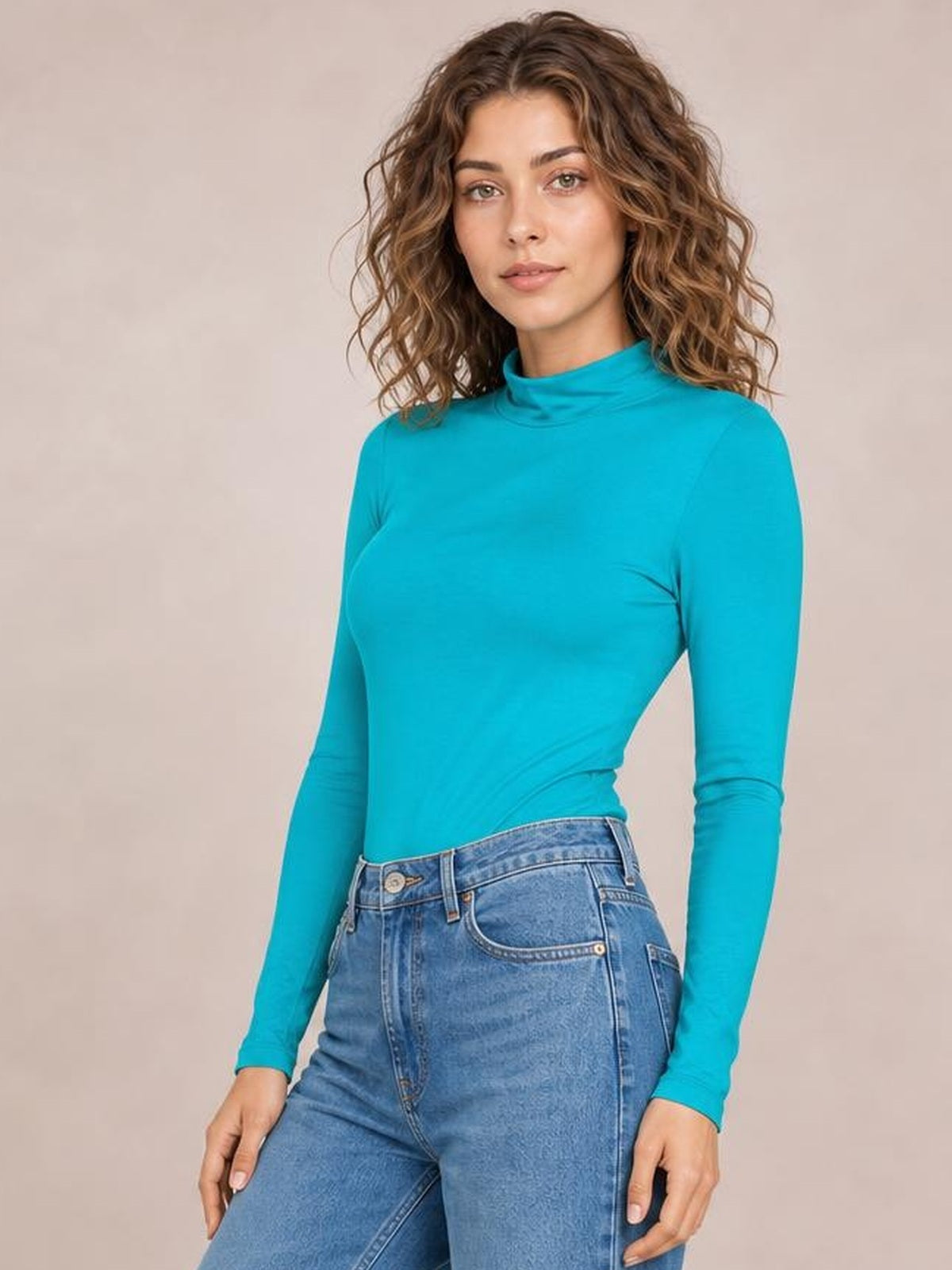 Model wears a turquoise mock neck long sleeve bodysuit with a fitted silhouette, opaque smooth construction, and moderate stretch, paired with jeans.