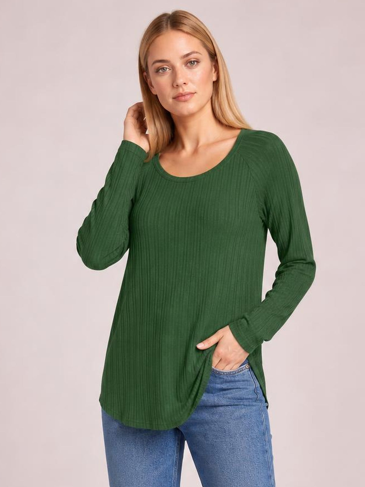 Model wears a forest green ribbed round neck slit T-shirt with long sleeves and a relaxed, elongated silhouette, posing with one hand at her hair.