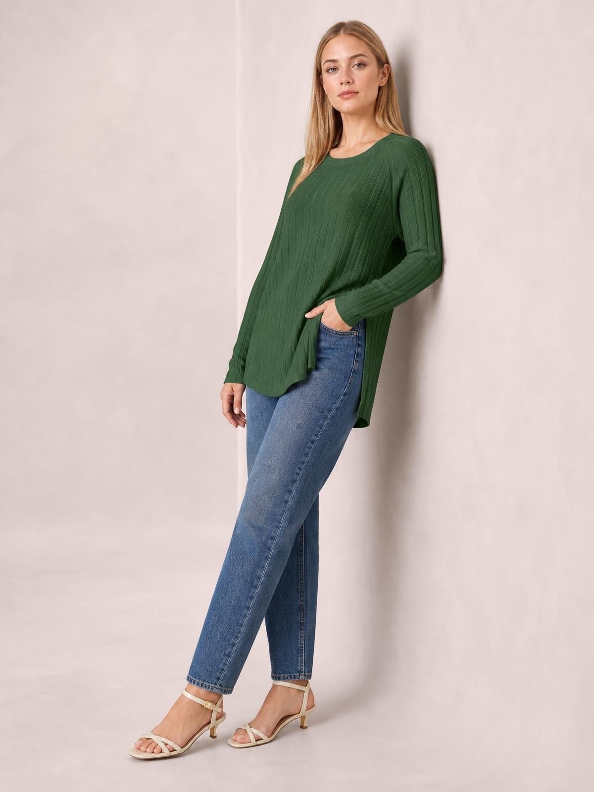 A model wears a forest green ribbed round-neck T-shirt with long sleeves and a side slit, posing casually with one hand at her jeans pocket.