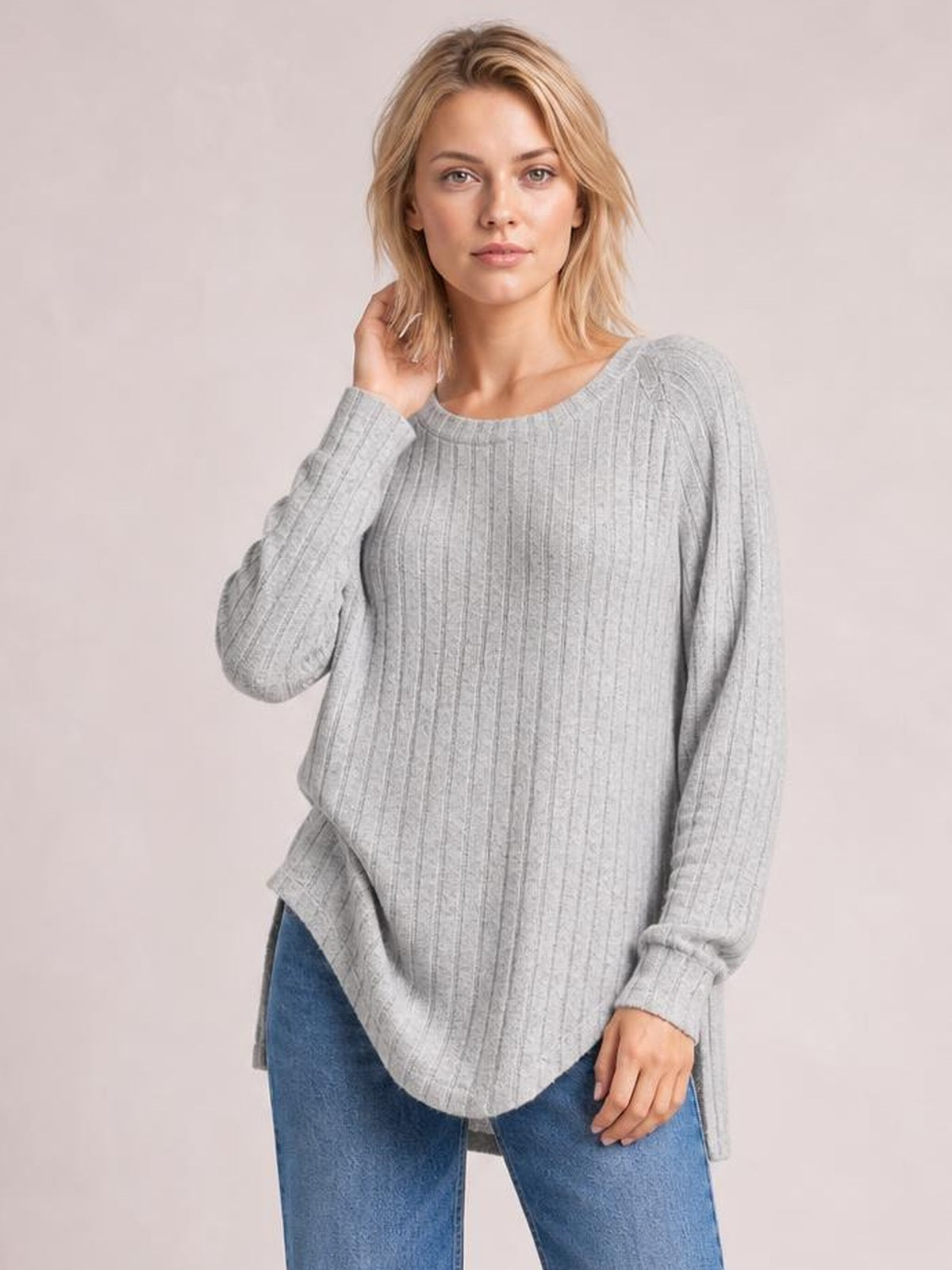 A model wears a light gray ribbed round neck slit T-shirt with long sleeves, a relaxed silhouette, and a curved hem, touching her hair.