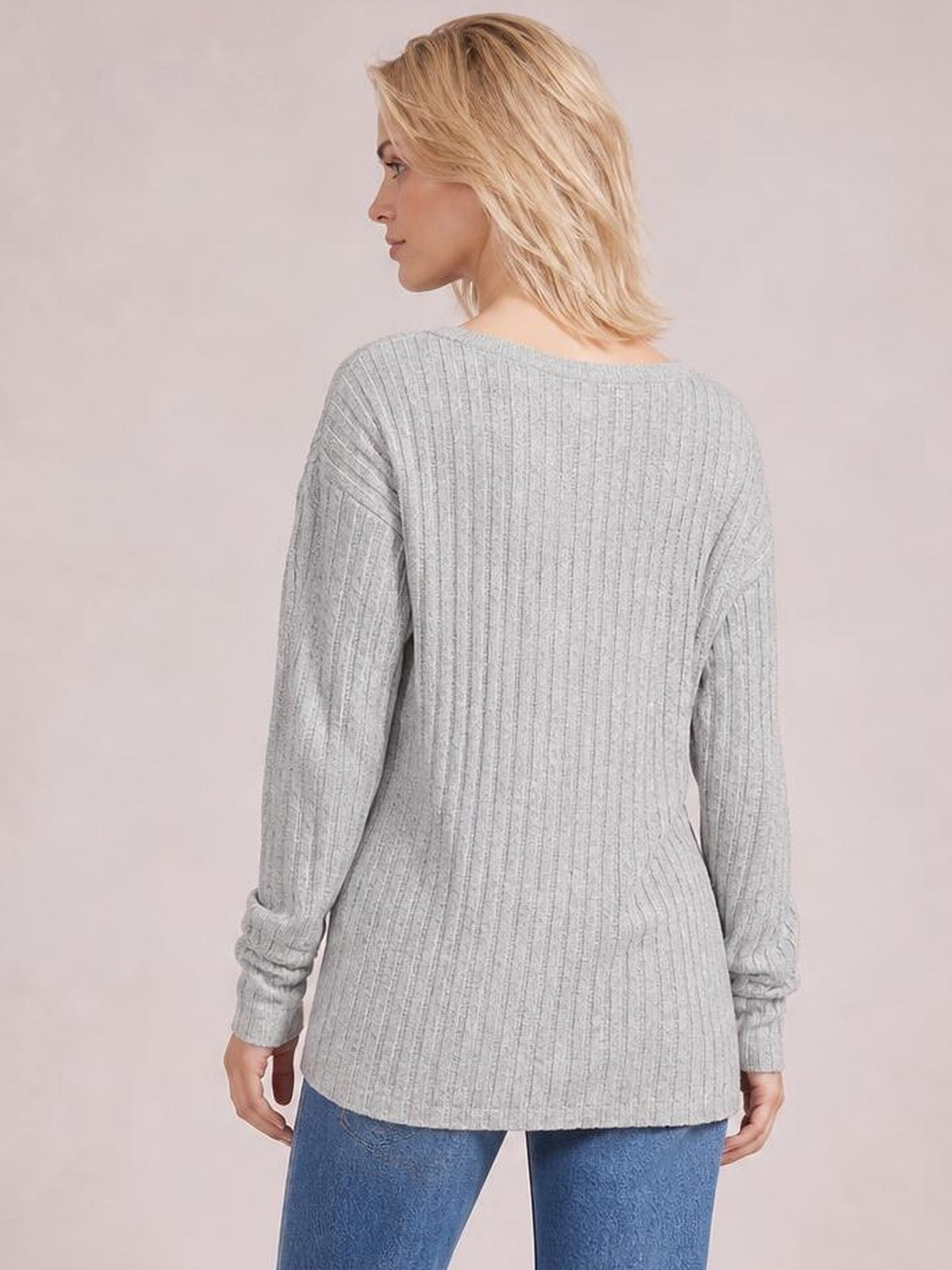 Model wears a light gray ribbed round-neck T-shirt with long sleeves and a relaxed straight silhouette, shown from the back while looking over her shoulder.