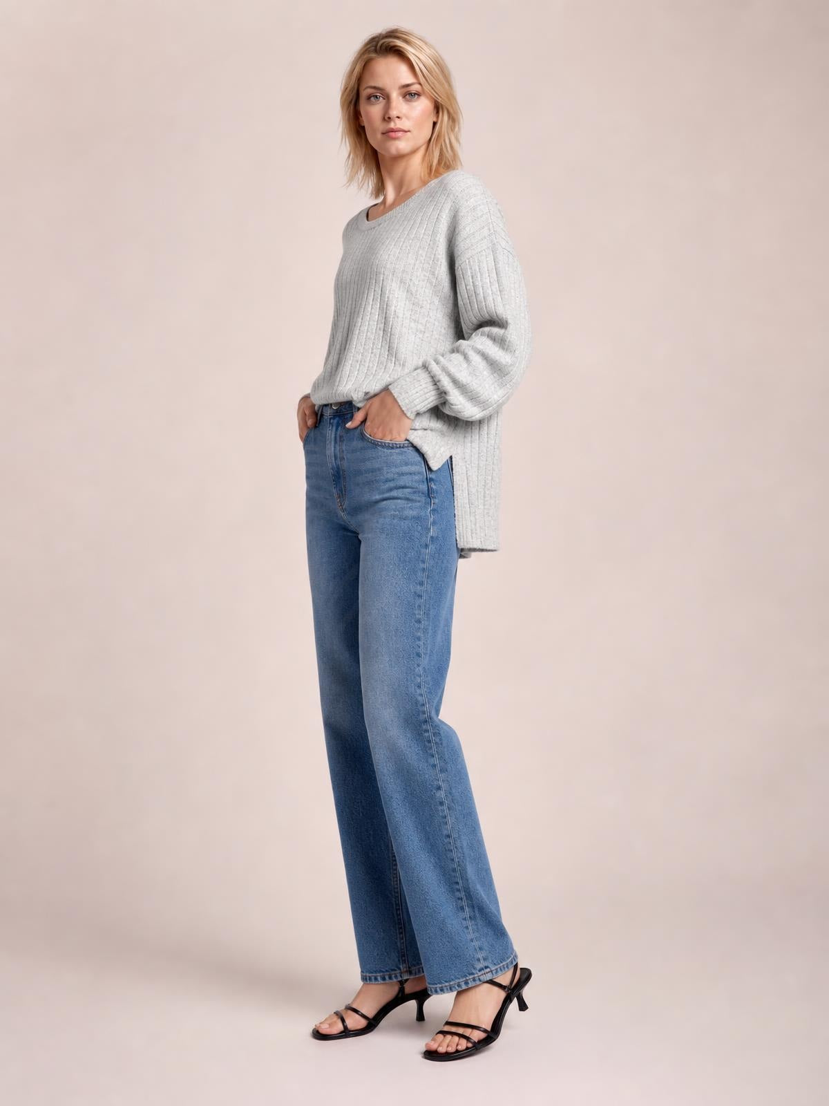 Model wears a gray ribbed round neck slit T-shirt with long sleeves and a relaxed tunic silhouette, posing with hands in her jeans pockets.