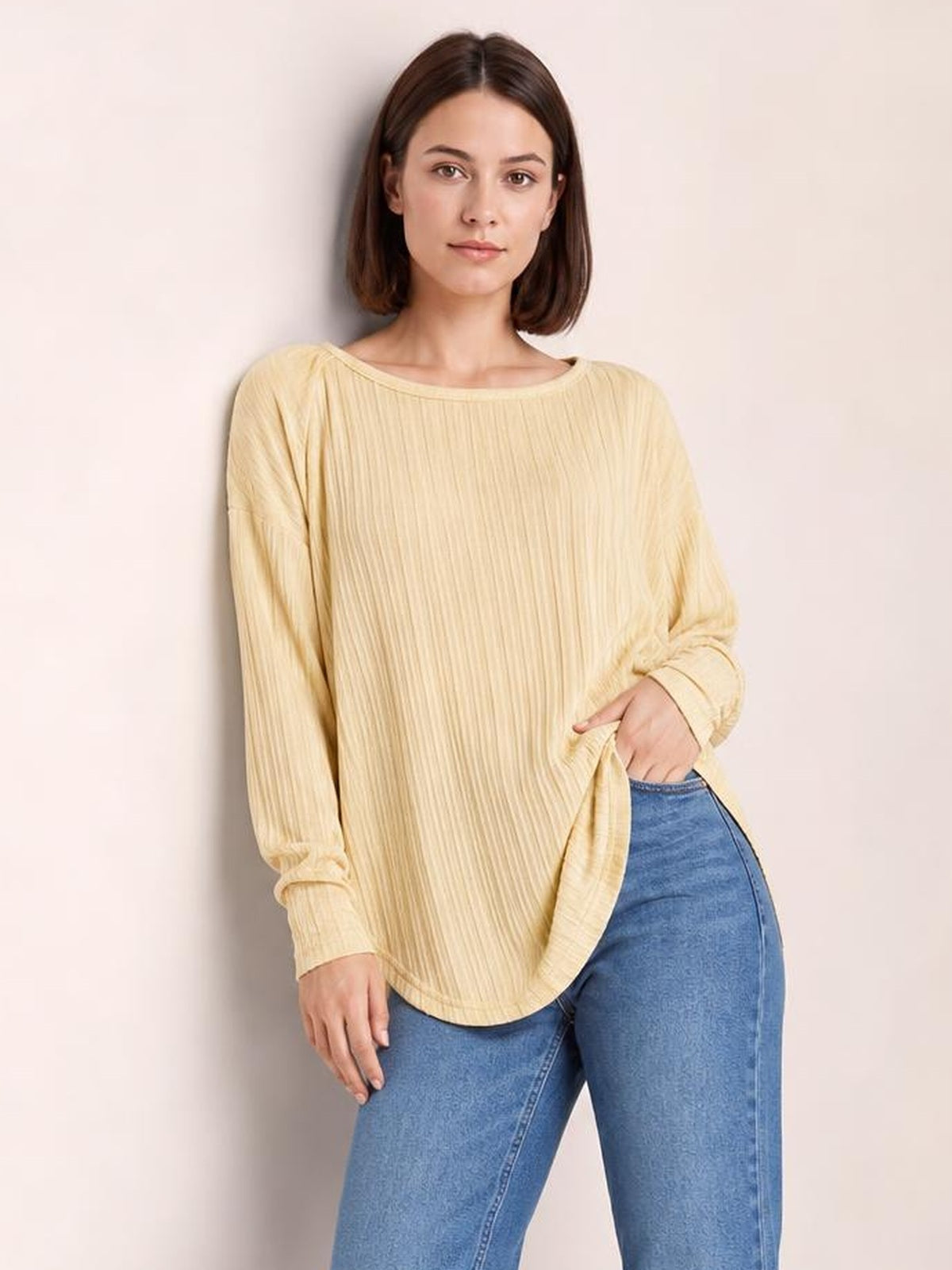 Model wears a pale yellow ribbed round neck slit T-shirt with long sleeves, a relaxed silhouette, curved hem, and one hand resting at the hip.