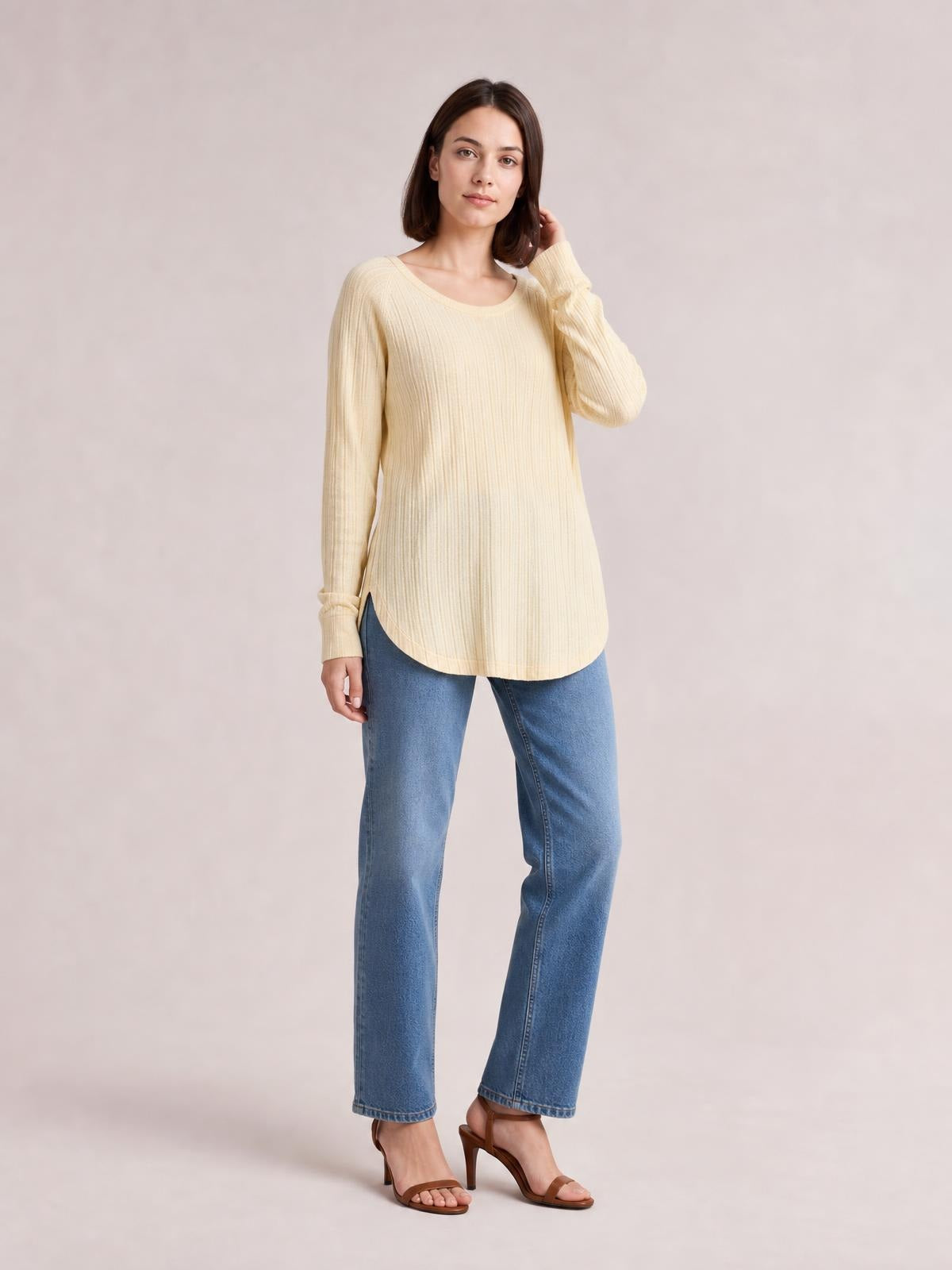 Model wearing a cream ribbed round neck slit T-shirt with long sleeves and a relaxed, curved hem silhouette, posing with one hand near her hair.
