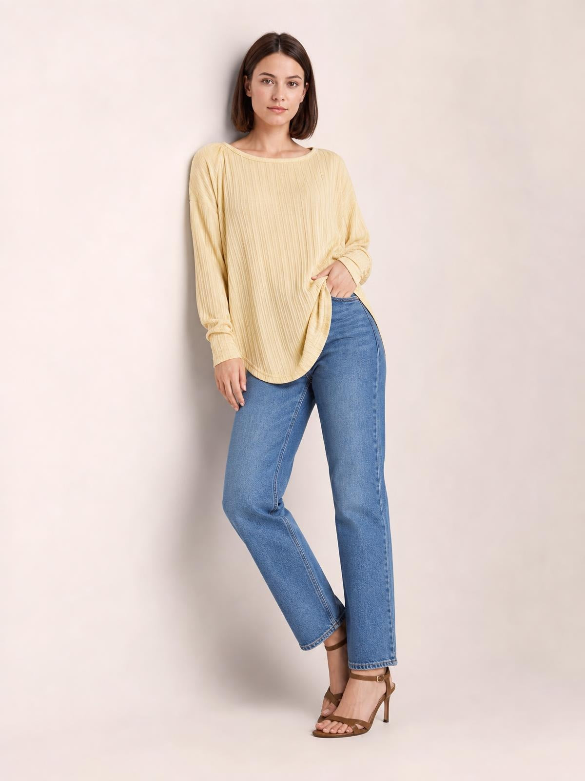 A model poses in a pale yellow ribbed round neck slit T-shirt with long sleeves, a relaxed silhouette, and a curved hem over blue jeans.