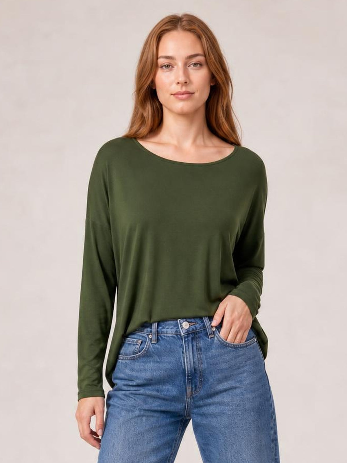 Model wearing an olive green round neck dropped shoulder T-shirt with long sleeves and a relaxed silhouette, standing with one hand in her jeans pocket.