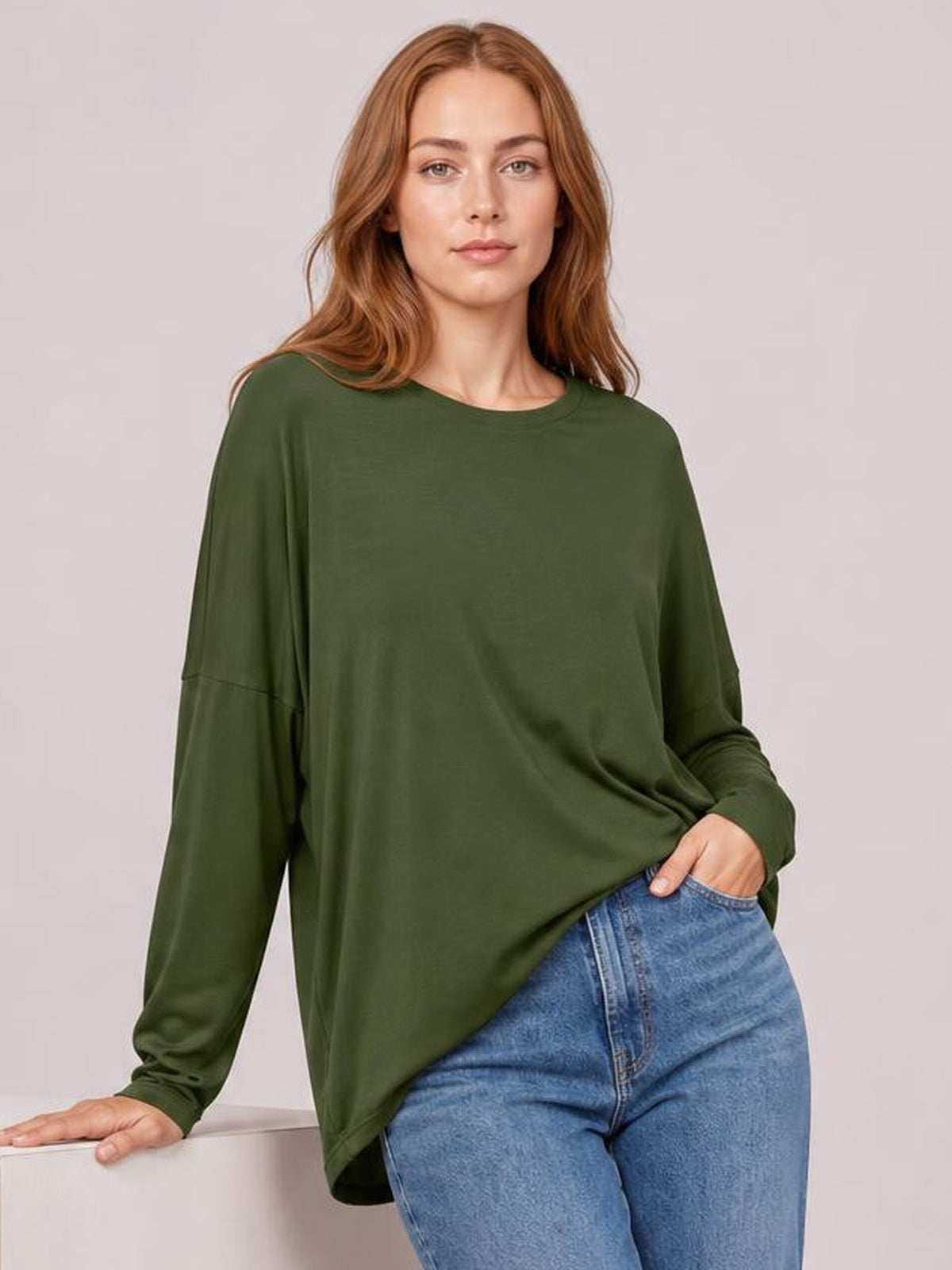 Model wearing a dark olive round-neck dropped-shoulder T-shirt with a relaxed long-sleeve silhouette, curved hem, and slightly stretchy drape.