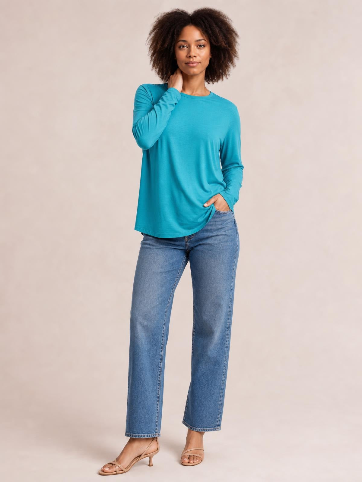 A model poses in a turquoise round neck dropped shoulder T-shirt with long sleeves and a relaxed, slightly loose silhouette, paired with jeans.