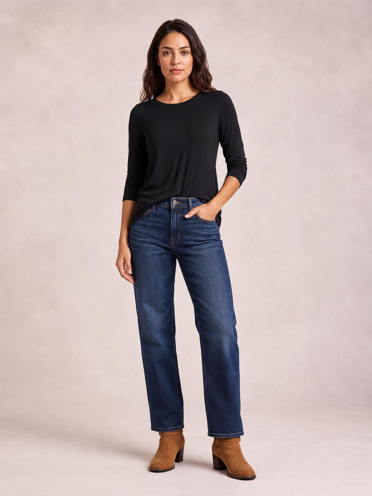 Model wearing a black round neck long sleeve top with a relaxed silhouette and subtle stretch, posed with one hand in her jeans pocket.