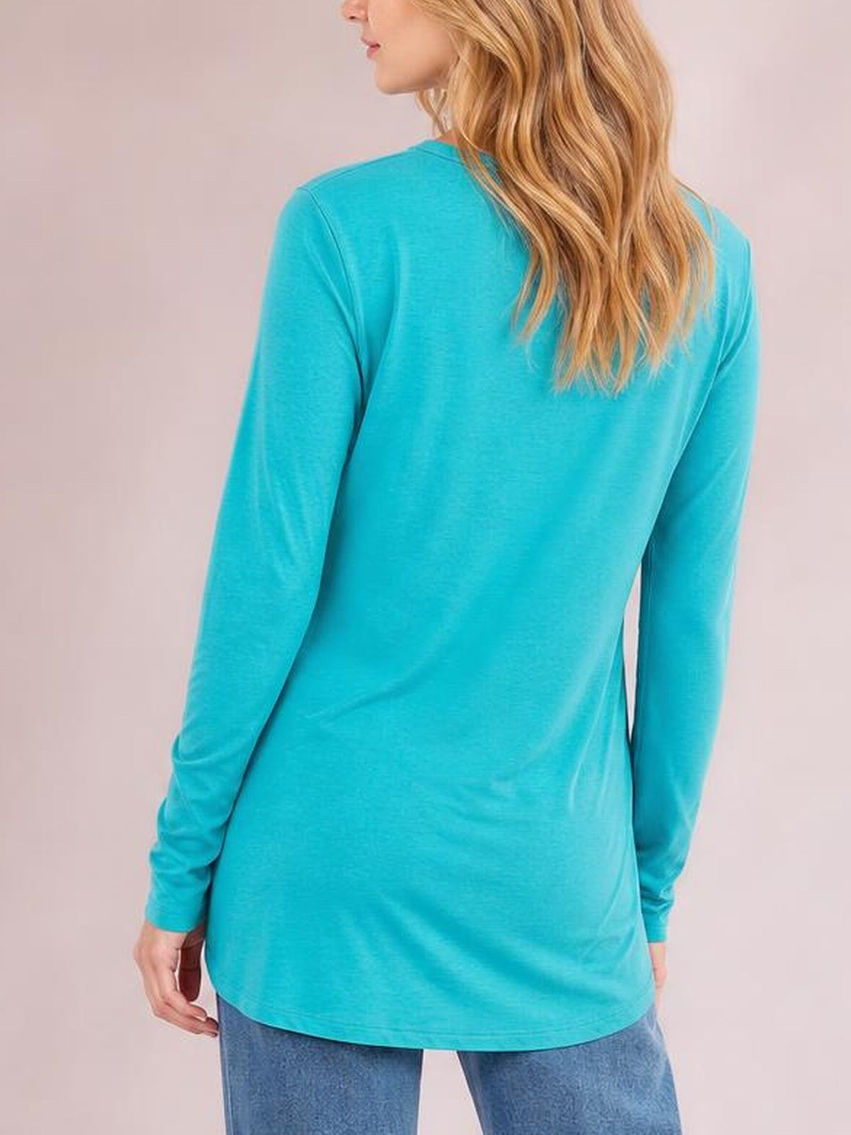 Model shown from behind wearing a bright turquoise round neck long sleeve top with a relaxed, slightly elongated silhouette and smooth construction.