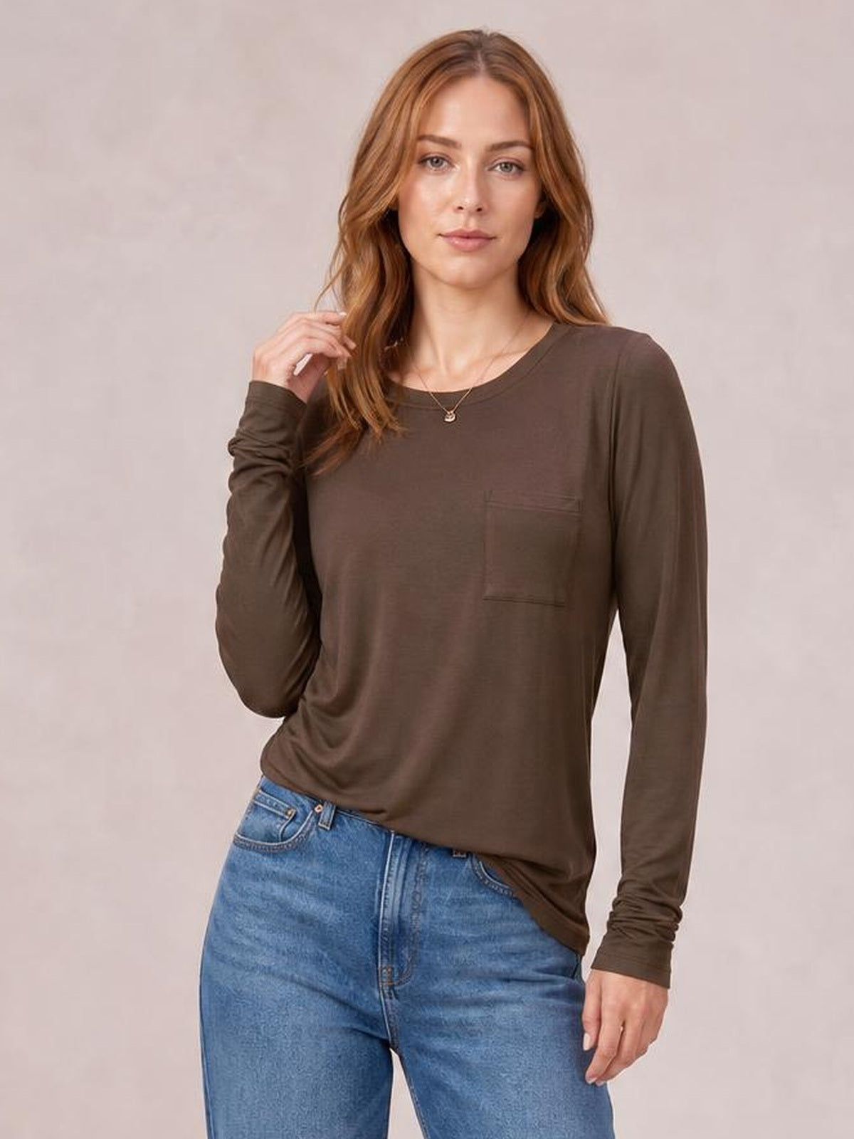 A model poses in a relaxed brown round neck long sleeve top with a straight silhouette, crew neckline, gathered cuffs, and a front chest pocket.