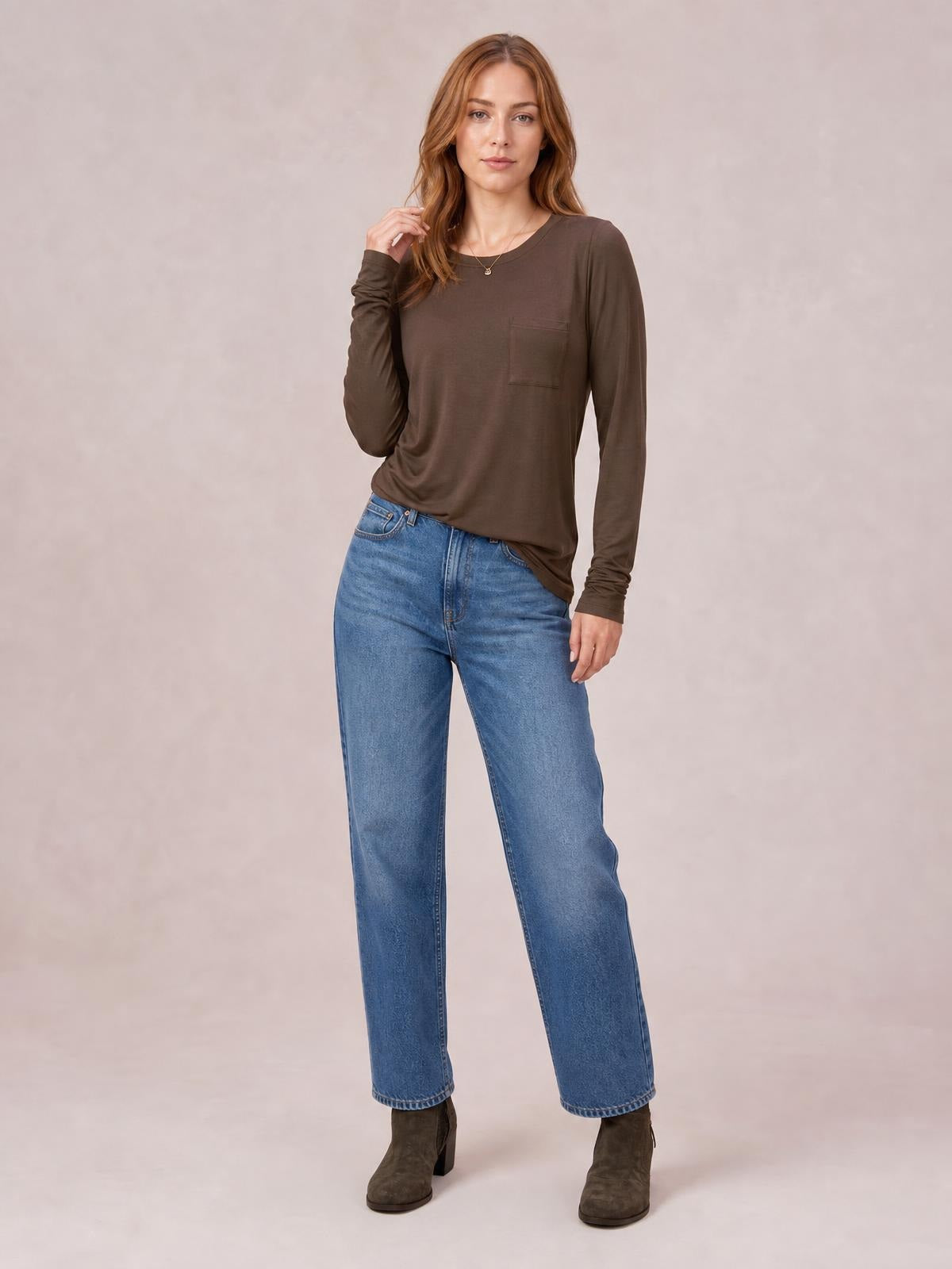 Model poses in a brown round neck long sleeve top with a relaxed silhouette, chest pocket, and slight stretch, paired with wide-leg jeans.