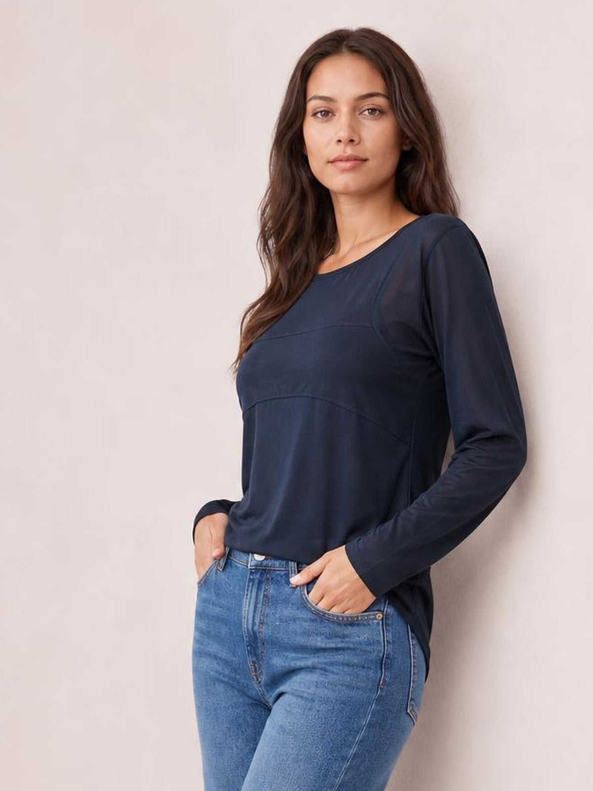 A model poses in a navy round neck long sleeve top with a relaxed silhouette, curved seam detailing, and a slightly longer hem over jeans.