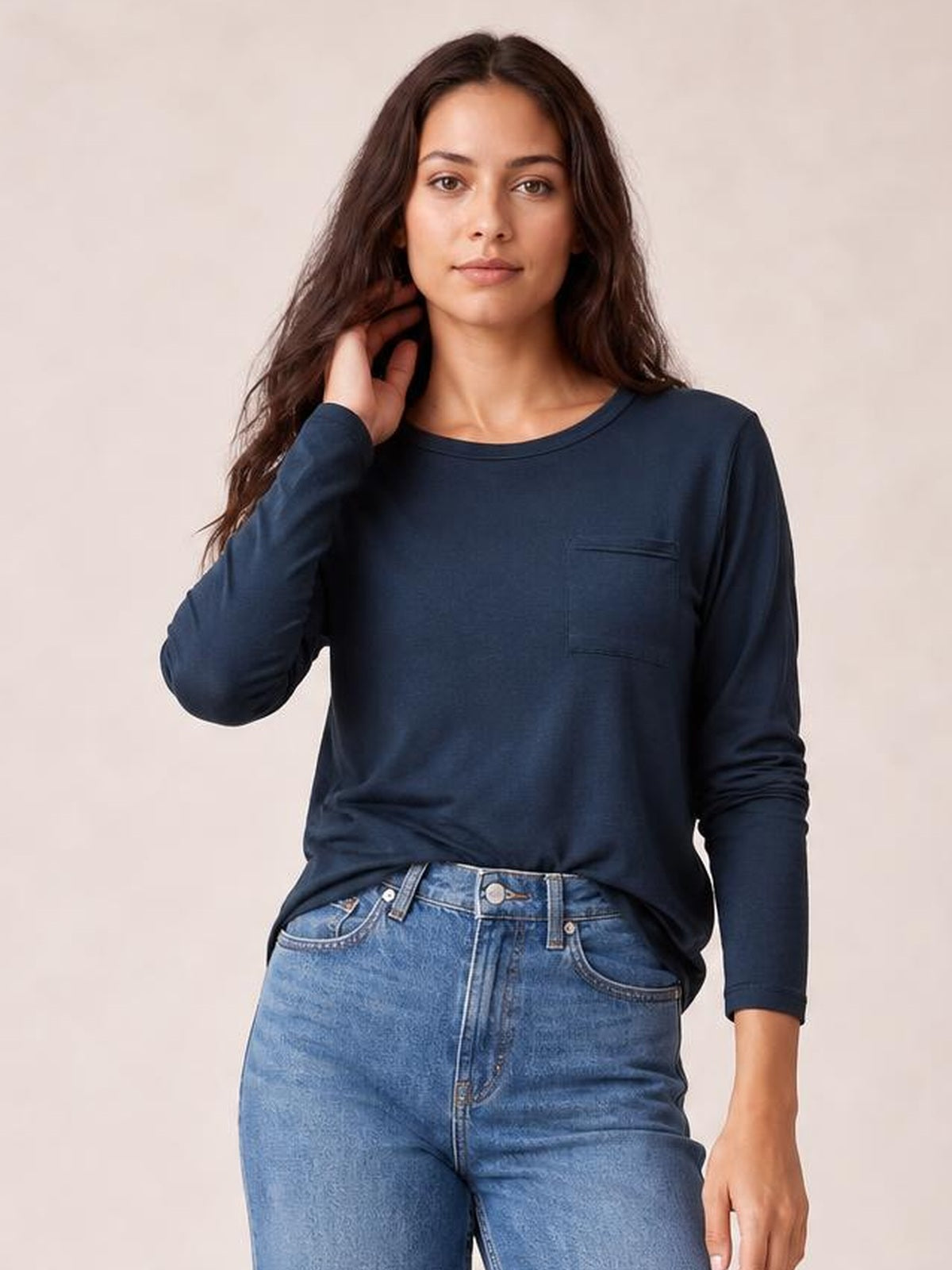 Model wears a dark navy round neck long sleeve top with a relaxed silhouette, visible chest pocket, and one hand resting near her hair.