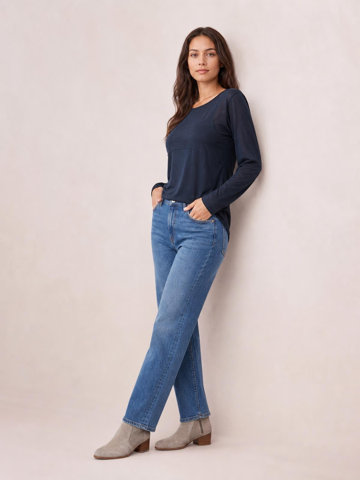 A model poses with one leg crossed, wearing a navy round neck long sleeve top with a relaxed silhouette and curved horizontal seam detailing.