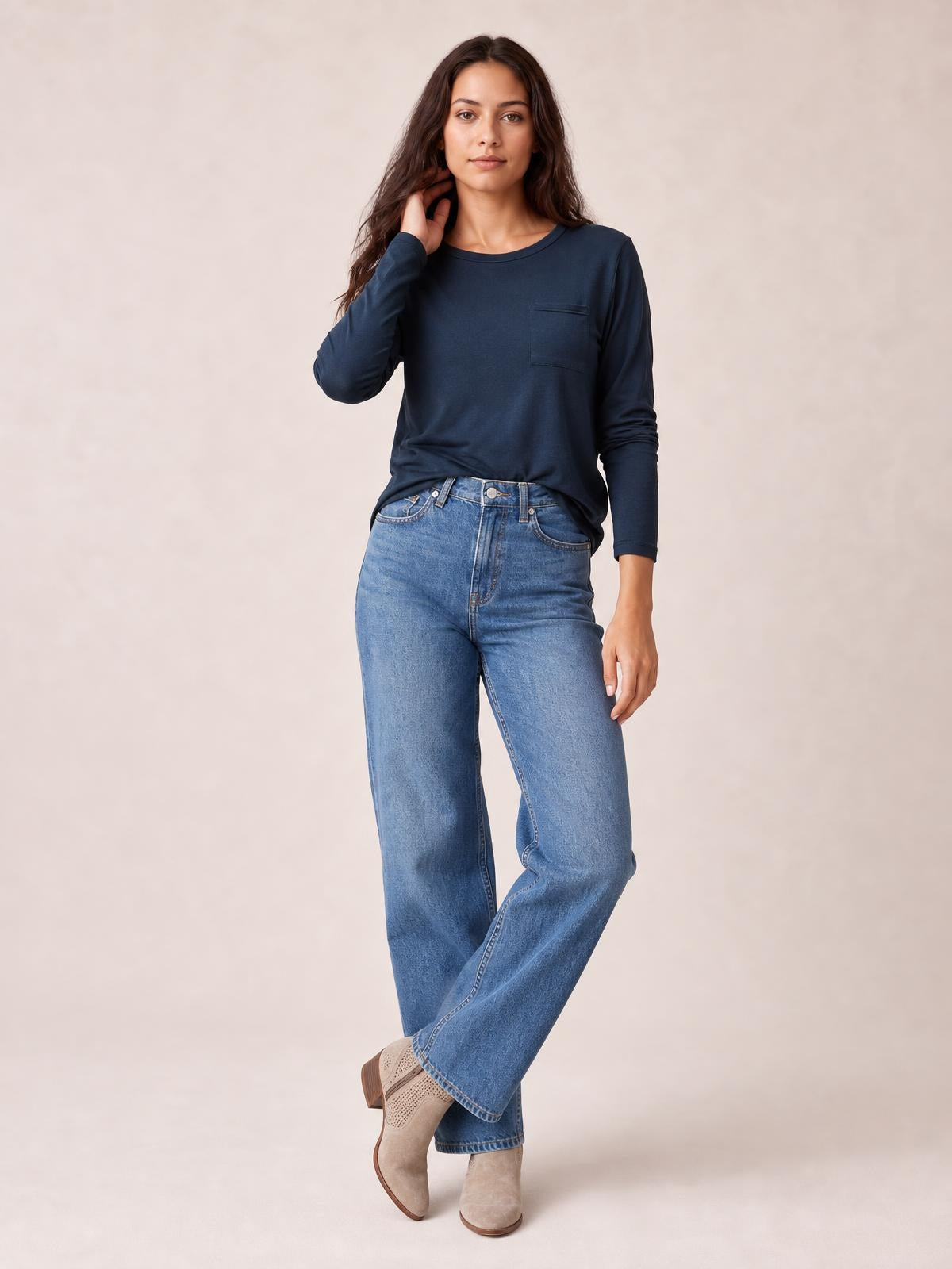 Model poses in a navy round neck long sleeve top with a relaxed silhouette and visible chest pocket, paired with wide-leg jeans.