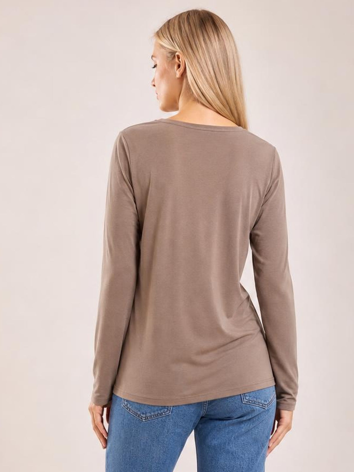 A woman faces away wearing a taupe round-neck long-sleeve top with a relaxed silhouette, smooth construction, and a straight hem over blue jeans.