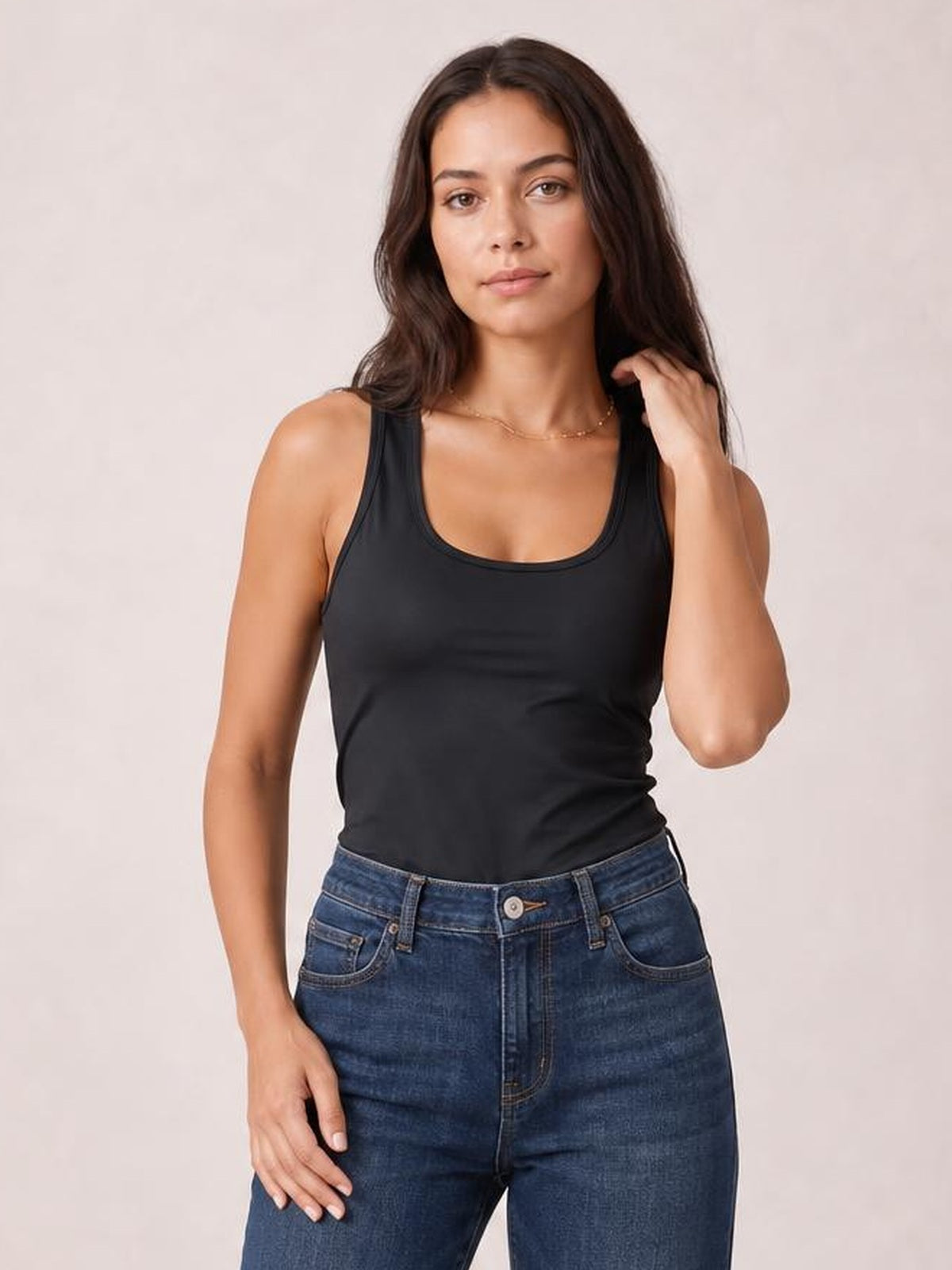 Model wears a black round neck racerback tank with a fitted silhouette and smooth bound neckline and armholes, posing with one hand in her hair.