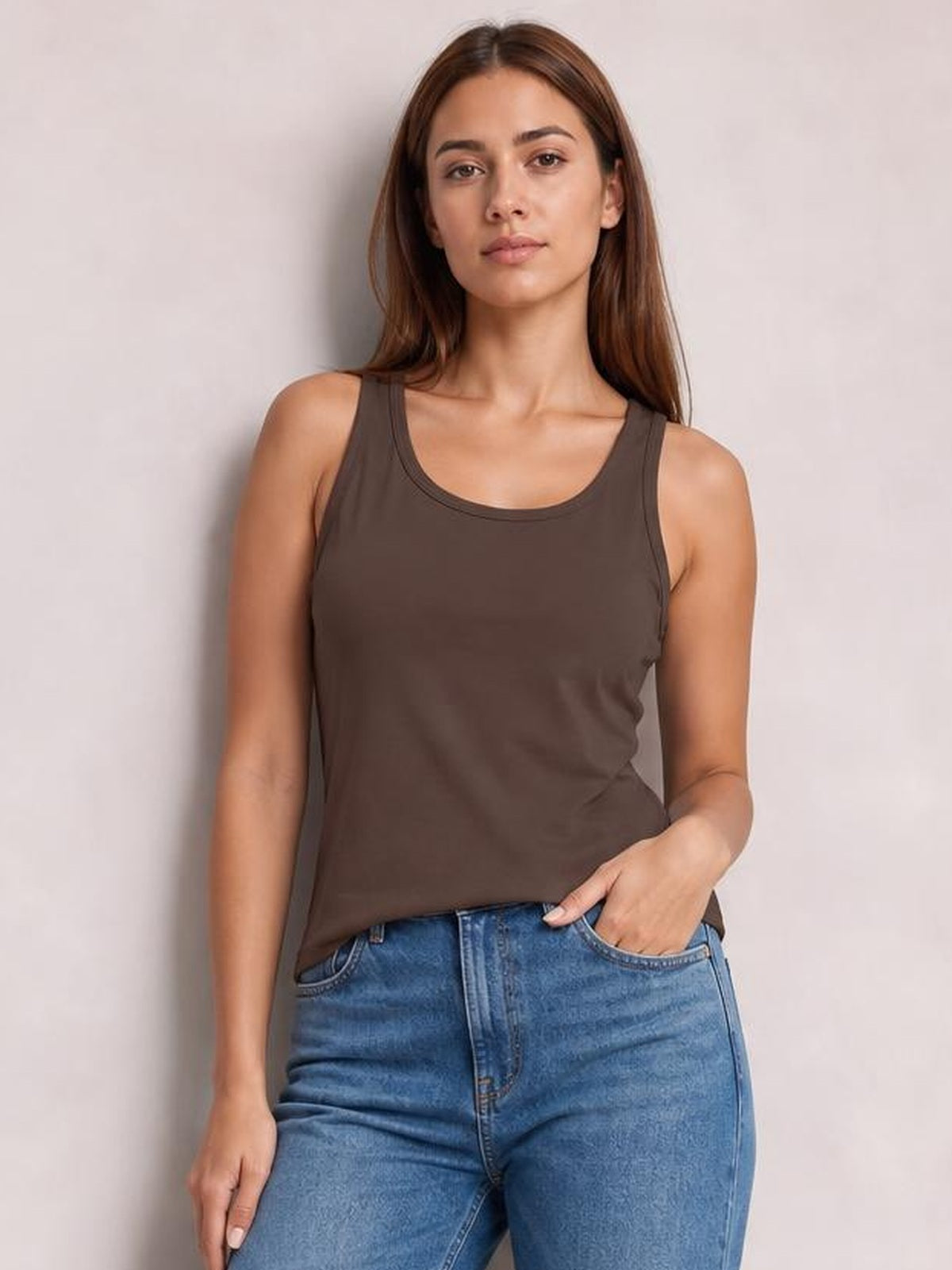 Model wearing a dark brown round neck racerback tank with wide shoulder straps and a relaxed, slightly fitted silhouette, paired with blue jeans.