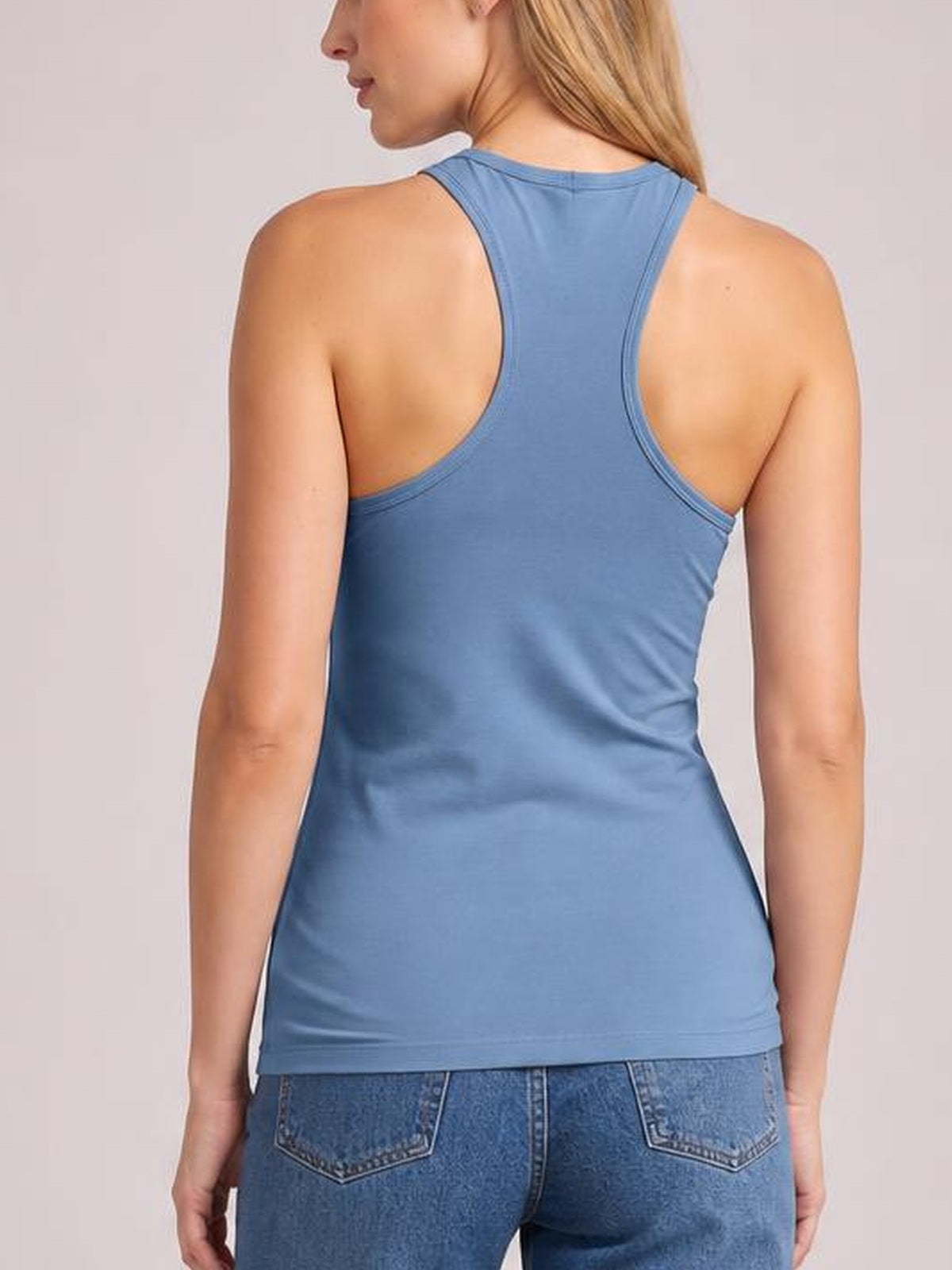 Model shown from the back wearing a blue round neck racerback tank with wide shoulder straps, curved armholes, and a fitted silhouette.