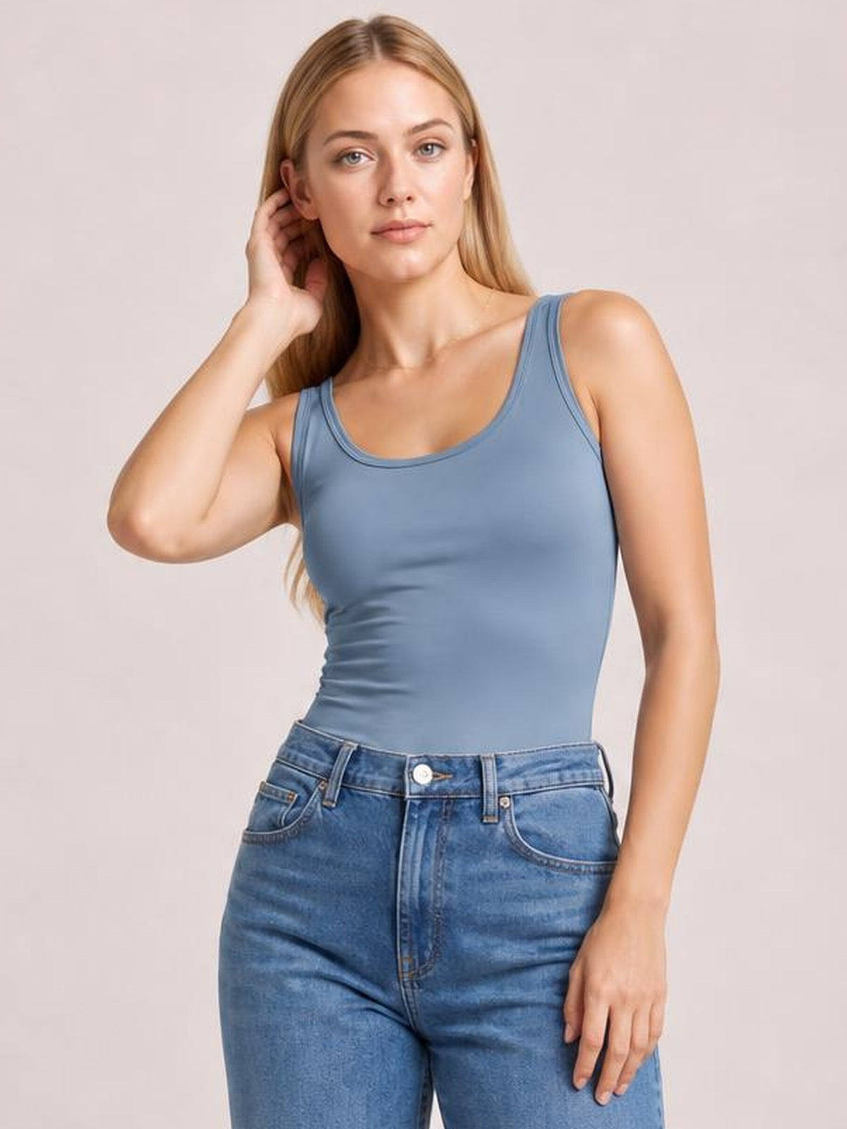Model poses in a blue round neck racerback tank with wide straps, a fitted silhouette, and subtle stretch, paired with jeans.