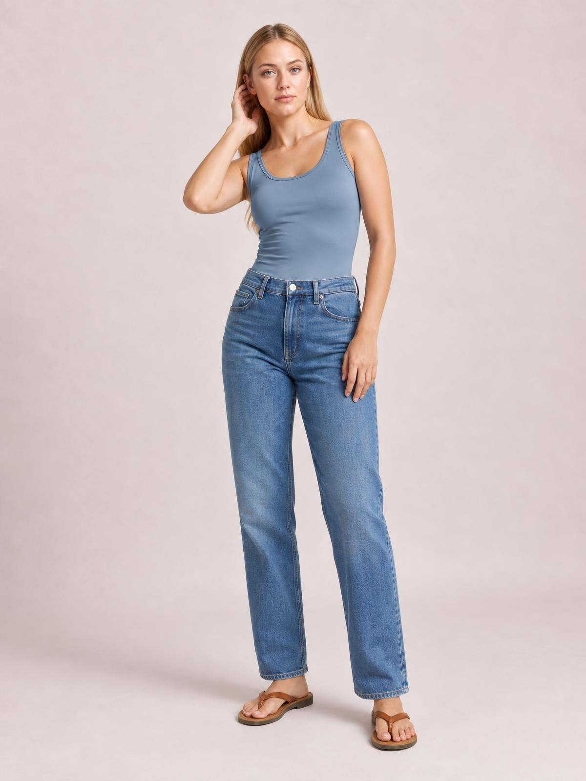 Model poses in a blue round neck racerback tank with wide shoulder straps and a fitted, slightly stretchy silhouette, paired with jeans.