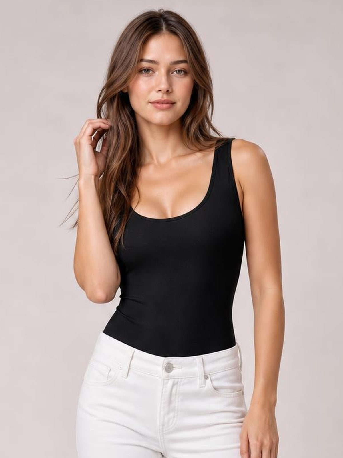 A model poses with one hand in her hair wearing a black round-neck bodysuit with wide shoulder straps and a smooth, fitted, opaque silhouette.