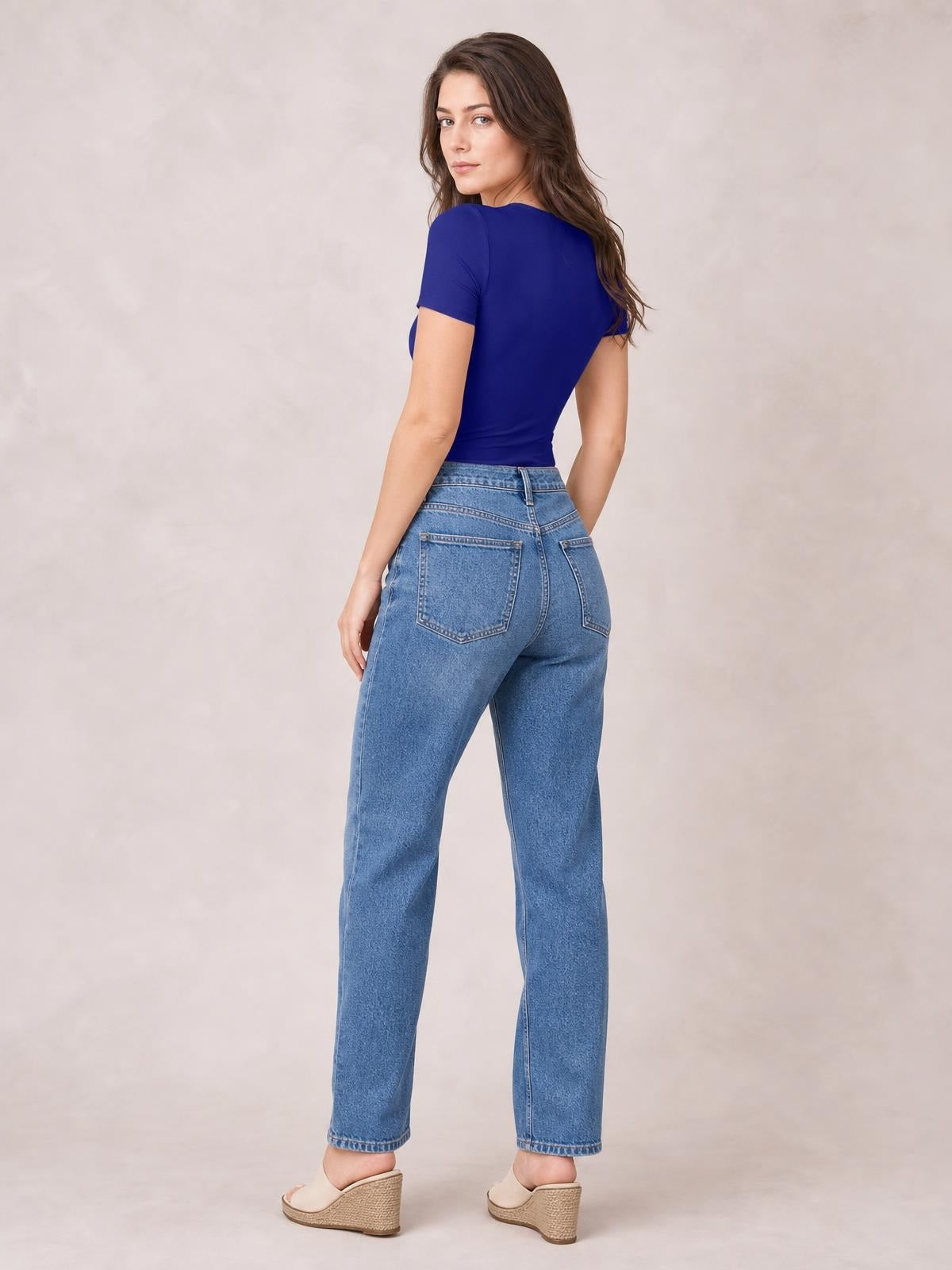 A model poses turned away in a cobalt blue round neck short sleeve bodysuit, showing its smooth, fitted silhouette and close-cut construction.
