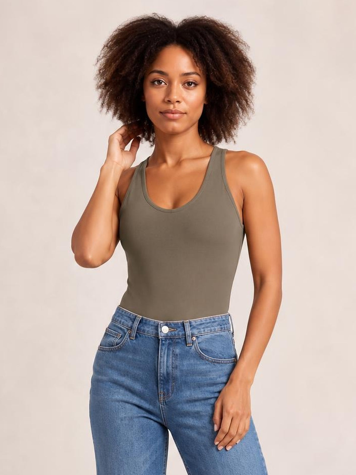 Model wears an olive green opaque bodysuit with a scoop neckline, sleeveless cut, smooth fitted silhouette, and moderate stretch while touching her hair.