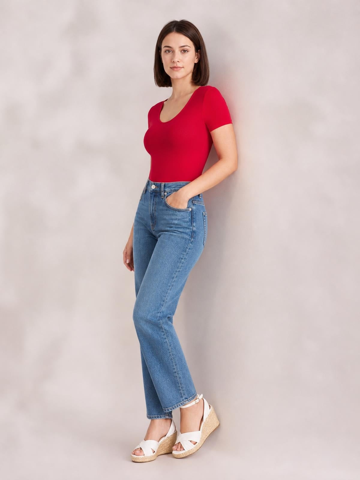 Model poses with one hand in her pocket wearing a fitted red round neck short sleeve bodysuit with an opaque, smooth silhouette.