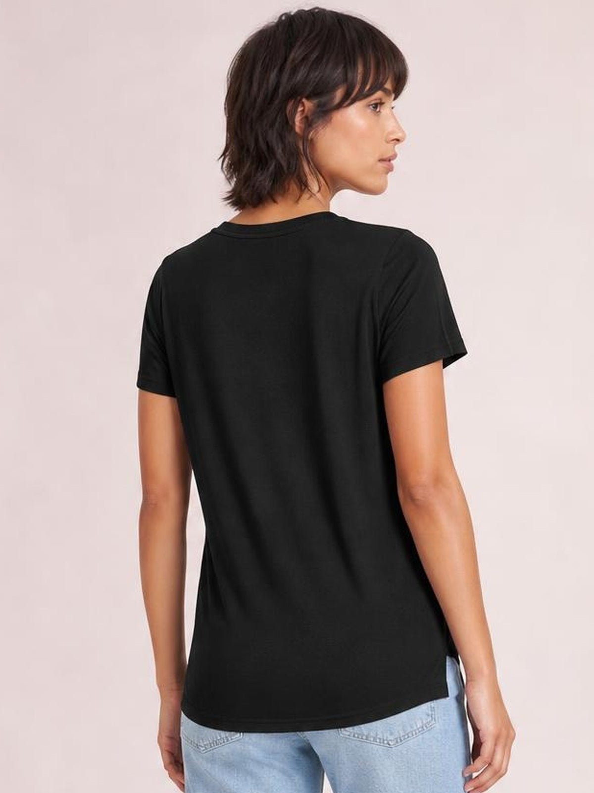 Model shown from behind wearing a black high-low T-shirt with short sleeves, a relaxed silhouette, curved hem, and visible side slit.