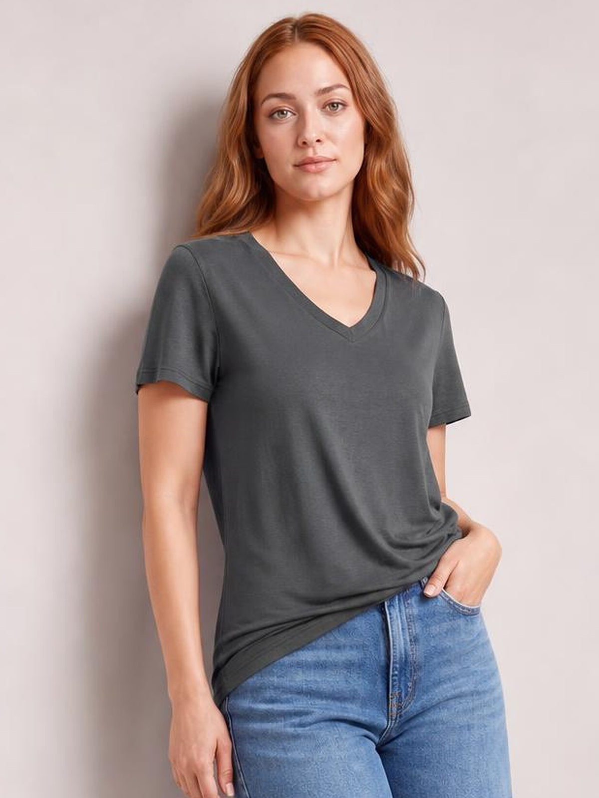 Model wearing a charcoal V-neck high-low T-shirt with short sleeves and a relaxed silhouette, posing with one hand in her jeans pocket.