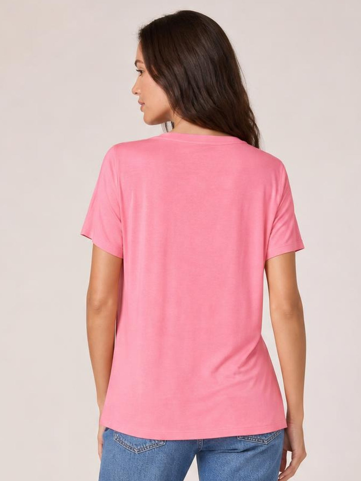 Model shown from the back in a slight side pose wearing a pink high-low T-shirt with short sleeves, relaxed silhouette, and side slit.