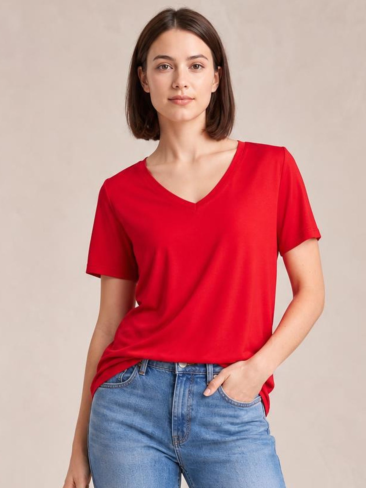Model wearing a red V-neck high-low T-shirt with short sleeves and a relaxed silhouette, posed with one hand in her jeans pocket.