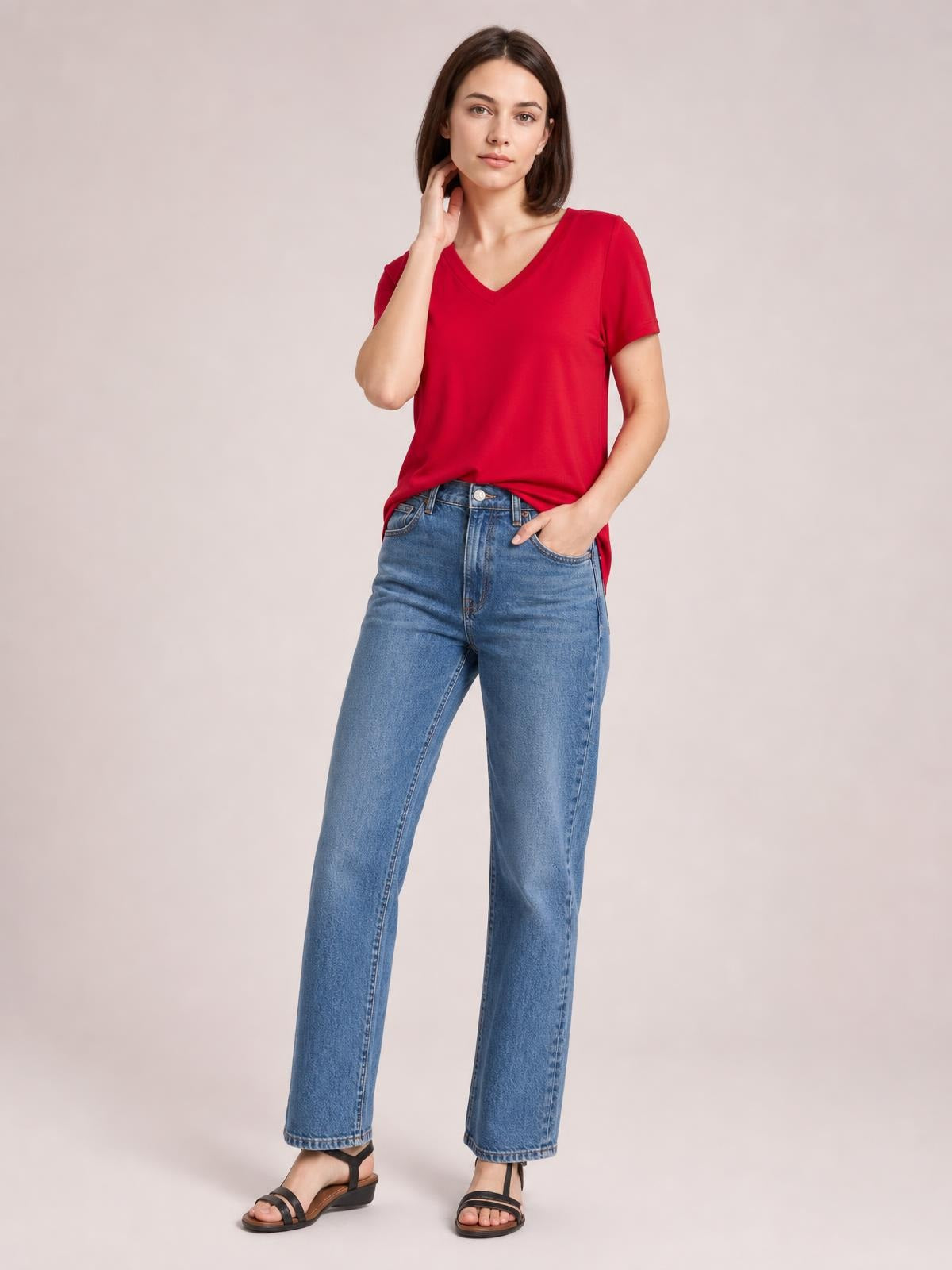 A model wears a red V-neck high-low T-shirt with short sleeves, a relaxed silhouette, and visible side slit while posing with one hand in her pocket.