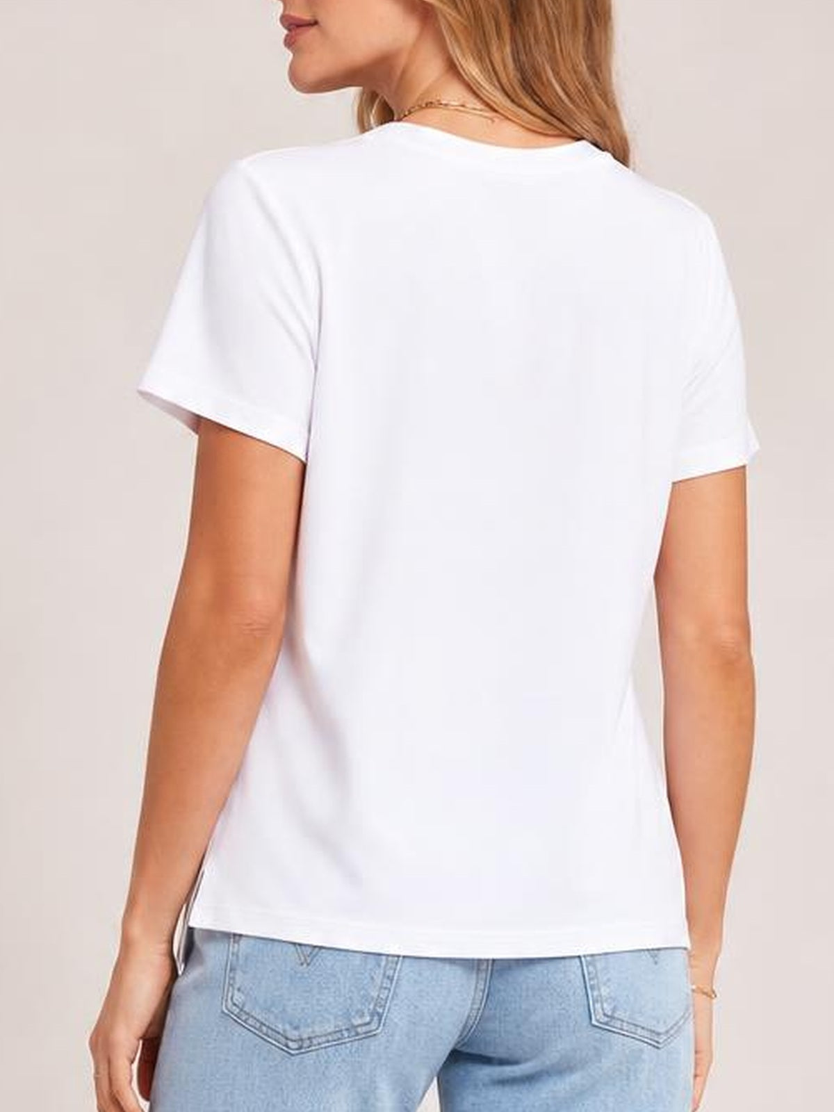 Model shown from the back wears a white high-low T-shirt with short sleeves, a relaxed silhouette, and a visible side slit at the hem.