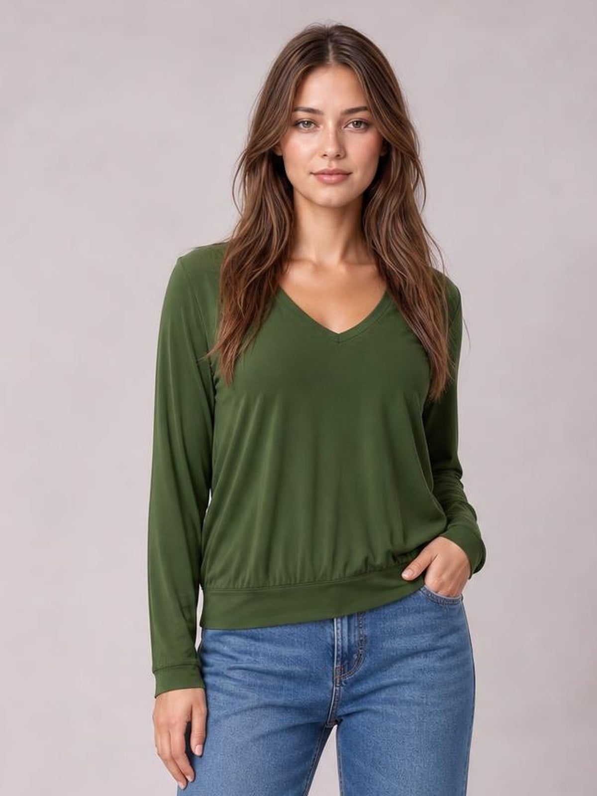 Model poses in a forest green V-neck top with long lantern sleeves, a relaxed silhouette, and a gathered elastic hem, paired with blue jeans.