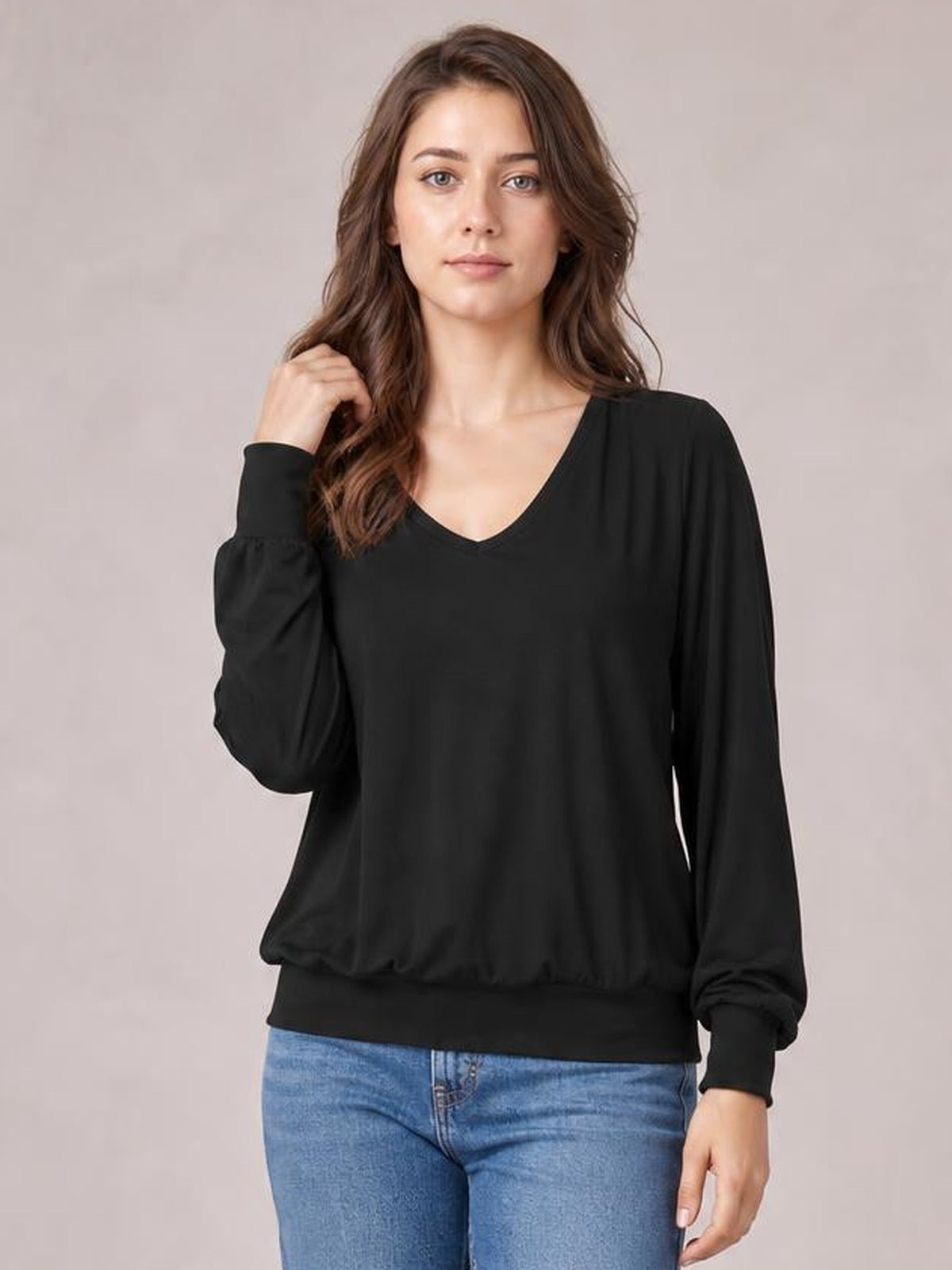 Model wearing a black V-neck lantern sleeve top with a relaxed silhouette, gathered cuffs, and a wide ribbed hem, posing with one hand near her hair.